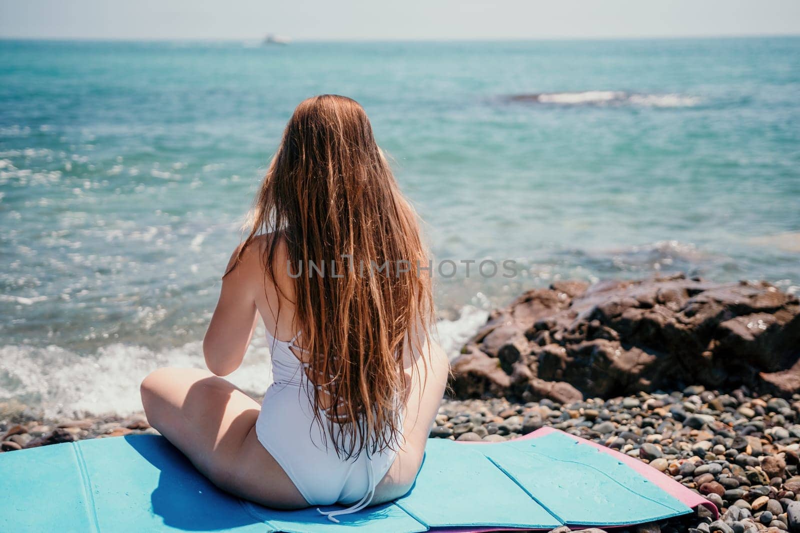 Woman yoga sea. Young woman with long hair in white swimsuit and boho style braclets practicing outdoors on yoga mat by the ocean on sunny day. Women's yoga fitness routine. Healthy lifestyle, harmony by panophotograph