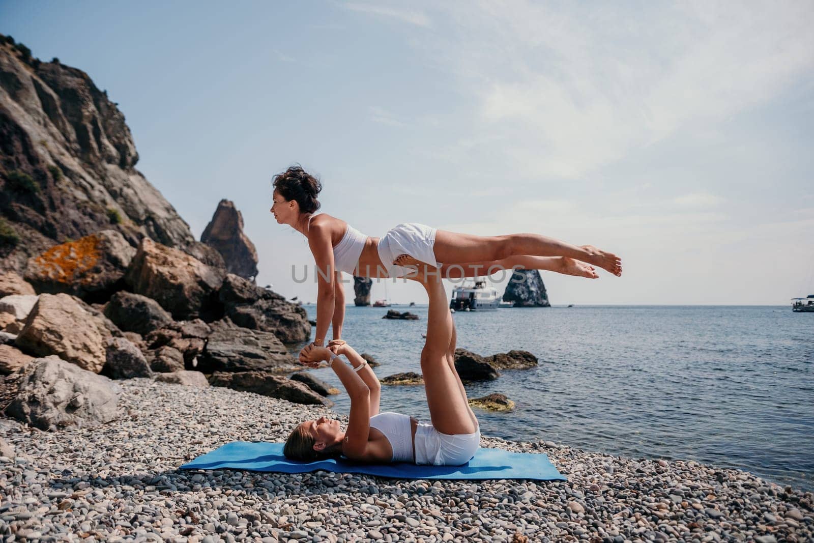 Woman sea yoga. Two Happy women meditating in yoga pose on the beach, ocean and rock mountains. Motivation and inspirational fit and exercising. Healthy lifestyle outdoors in nature, fitness concept. by panophotograph