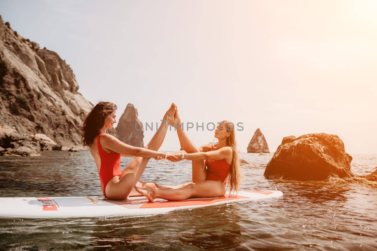 Woman sup yoga. Middle age sporty woman practising yoga pilates on paddle sup surfboard. Female stretching doing workout on sea water. Modern individual hipster outdoor summer sport activity