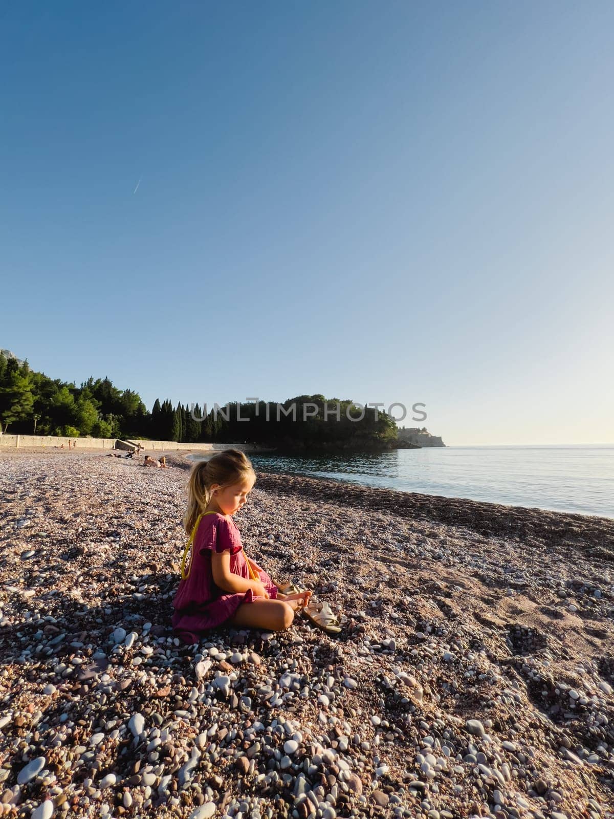 Little girl sitting on a pebble beach by the sea. High quality photo