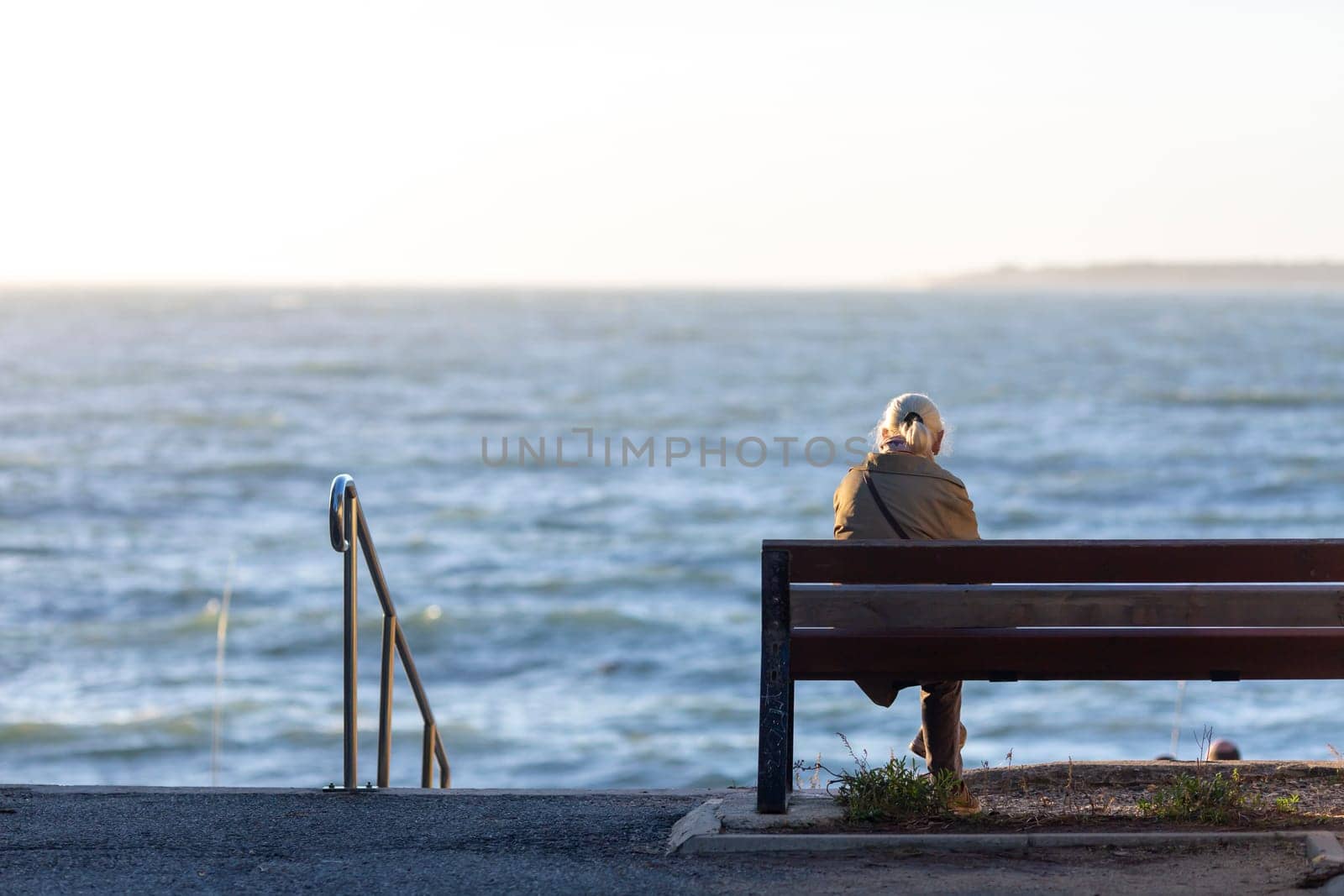Back view of senior woman sitting on a bench at the beach by lhorintson