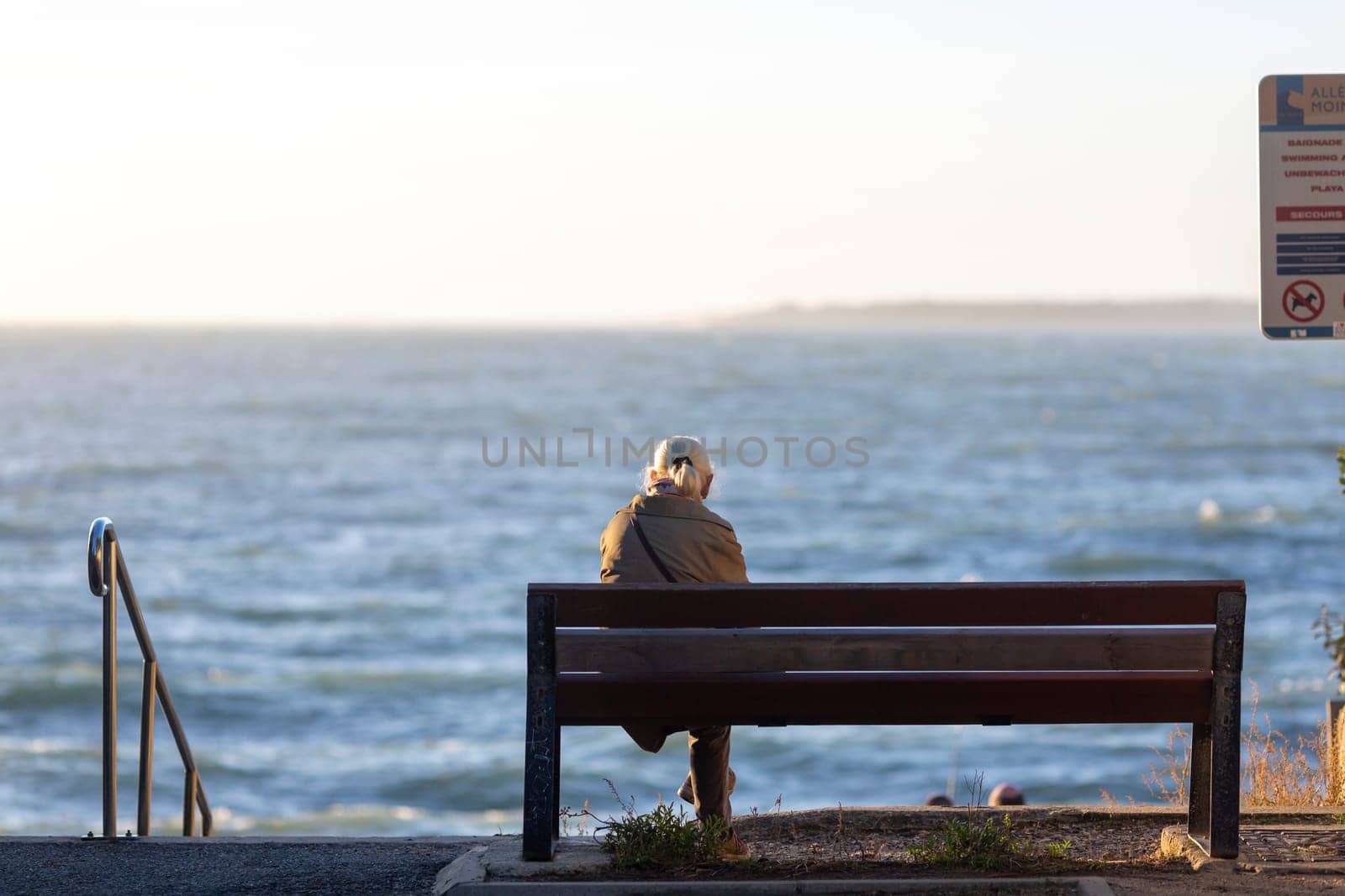 Back view of senior woman sitting on a bench at the beach by lhorintson