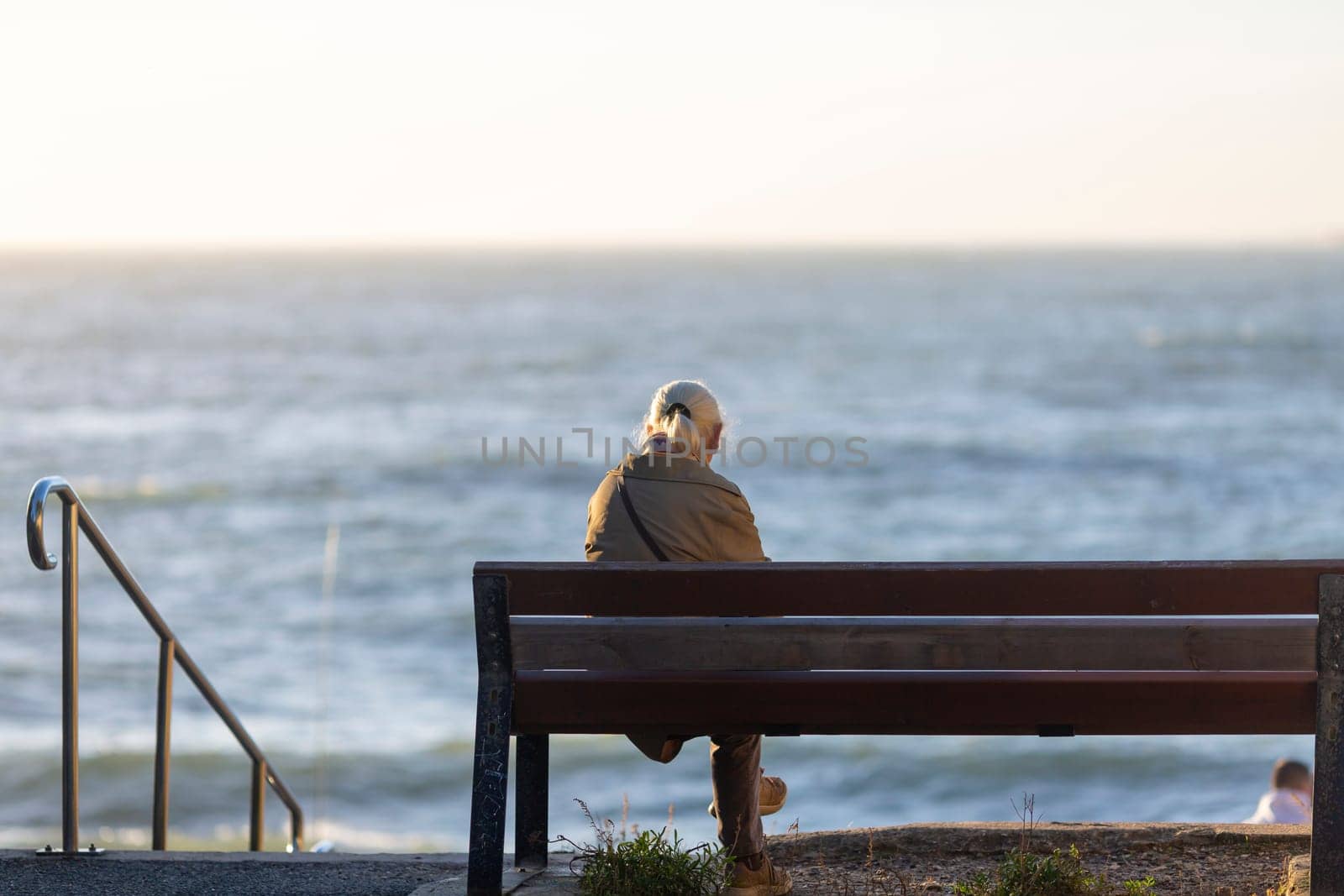 Back view of senior woman sitting on a bench at the beach by lhorintson