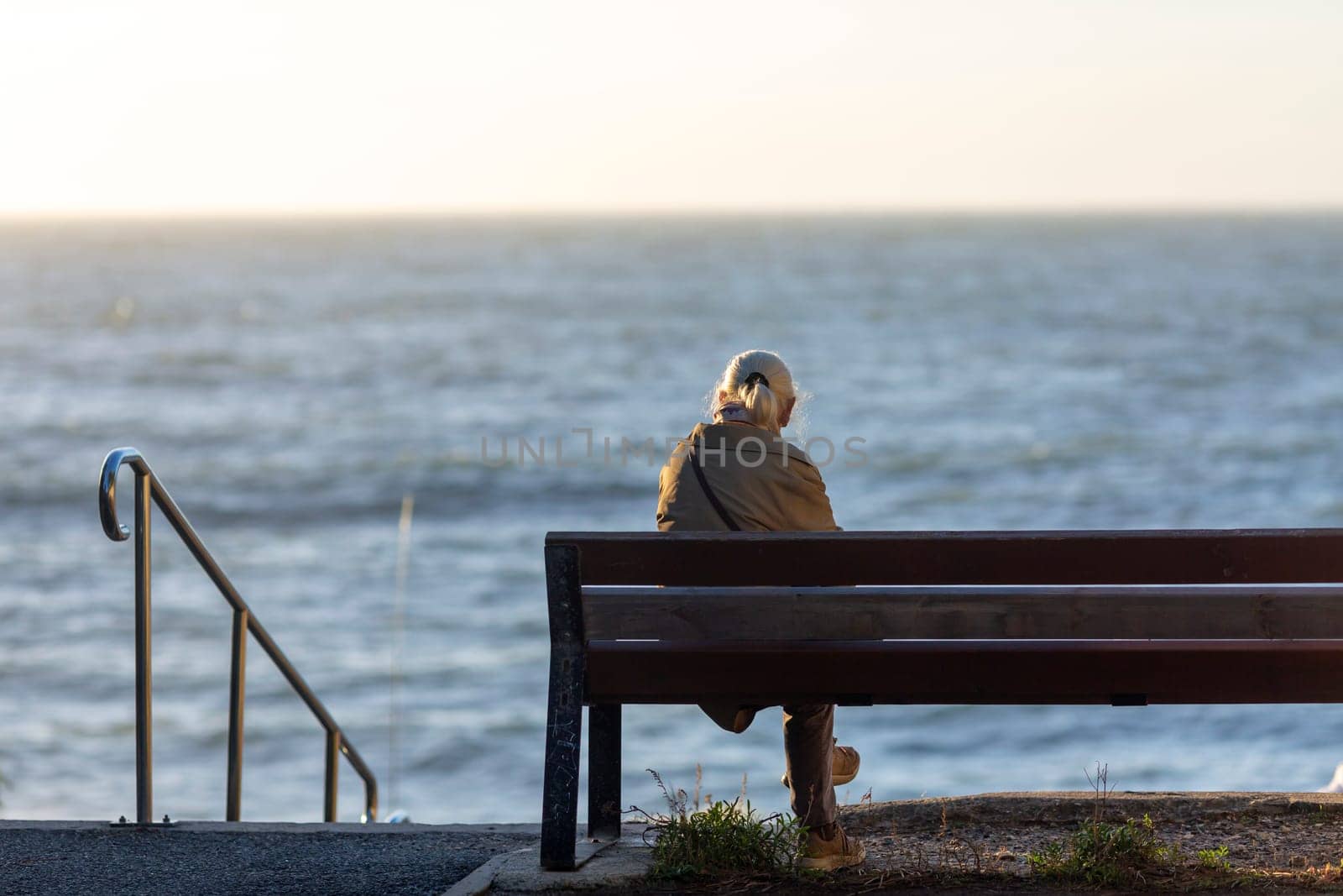 Back view of senior woman sitting on a bench at the beach a sunny day