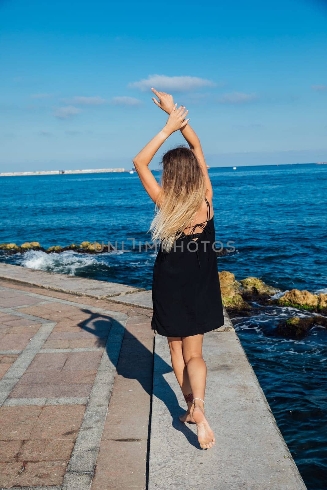 Beautiful slender woman in black summer dress on the seashore by Simakov