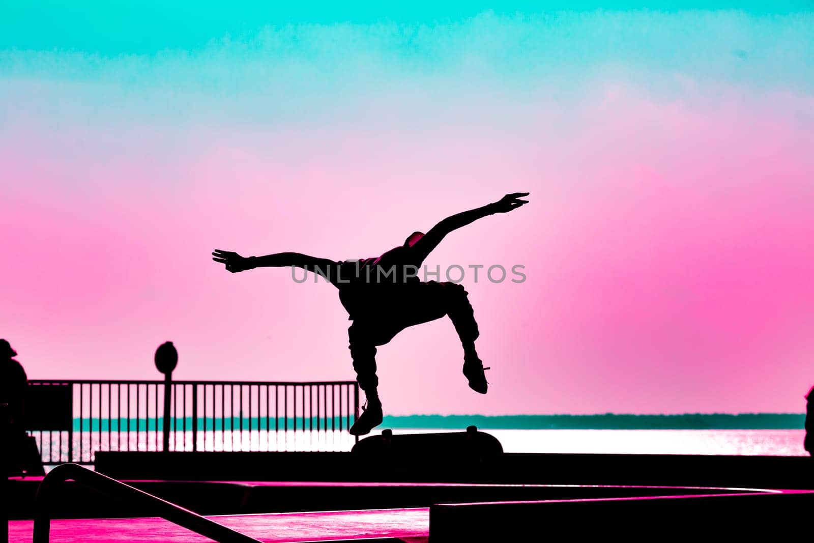 Unrecognizable teenage boy silhouette showing high jump tricks on scooter against orange sunsetwarm sky at skatepark. Sport, extreme, freestyle, outdoor activity concept