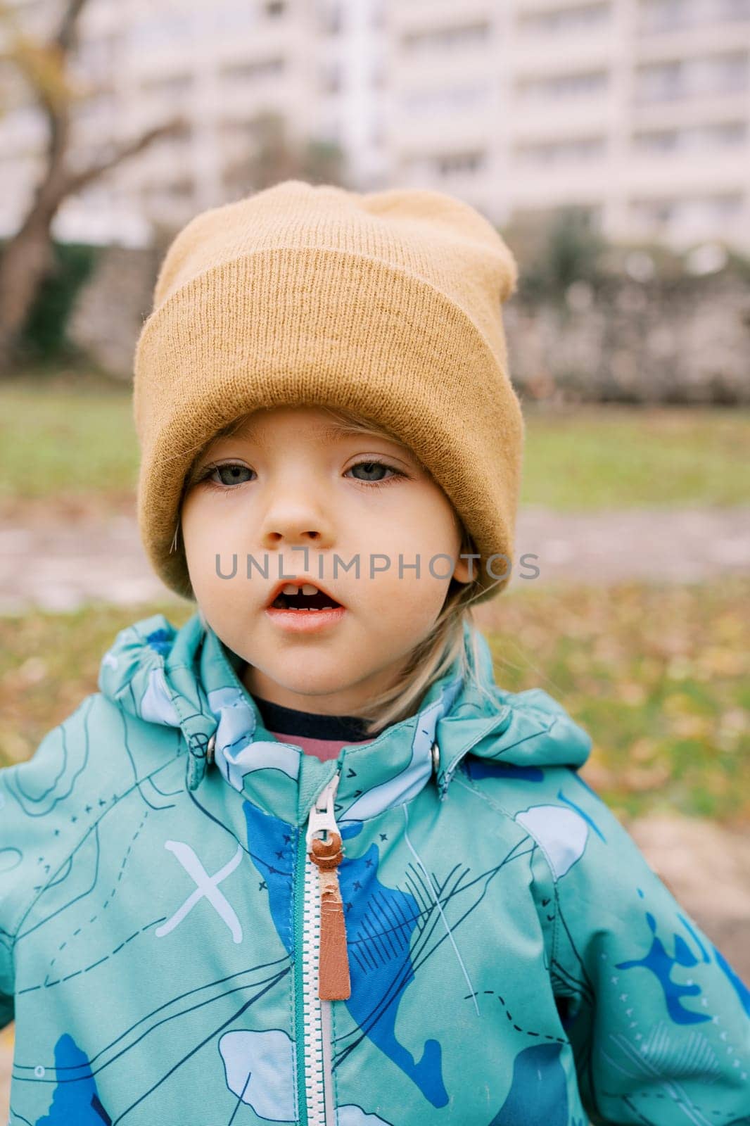 Little girl in jacket and a hat stands in the garden with her mouth open. High quality photo
