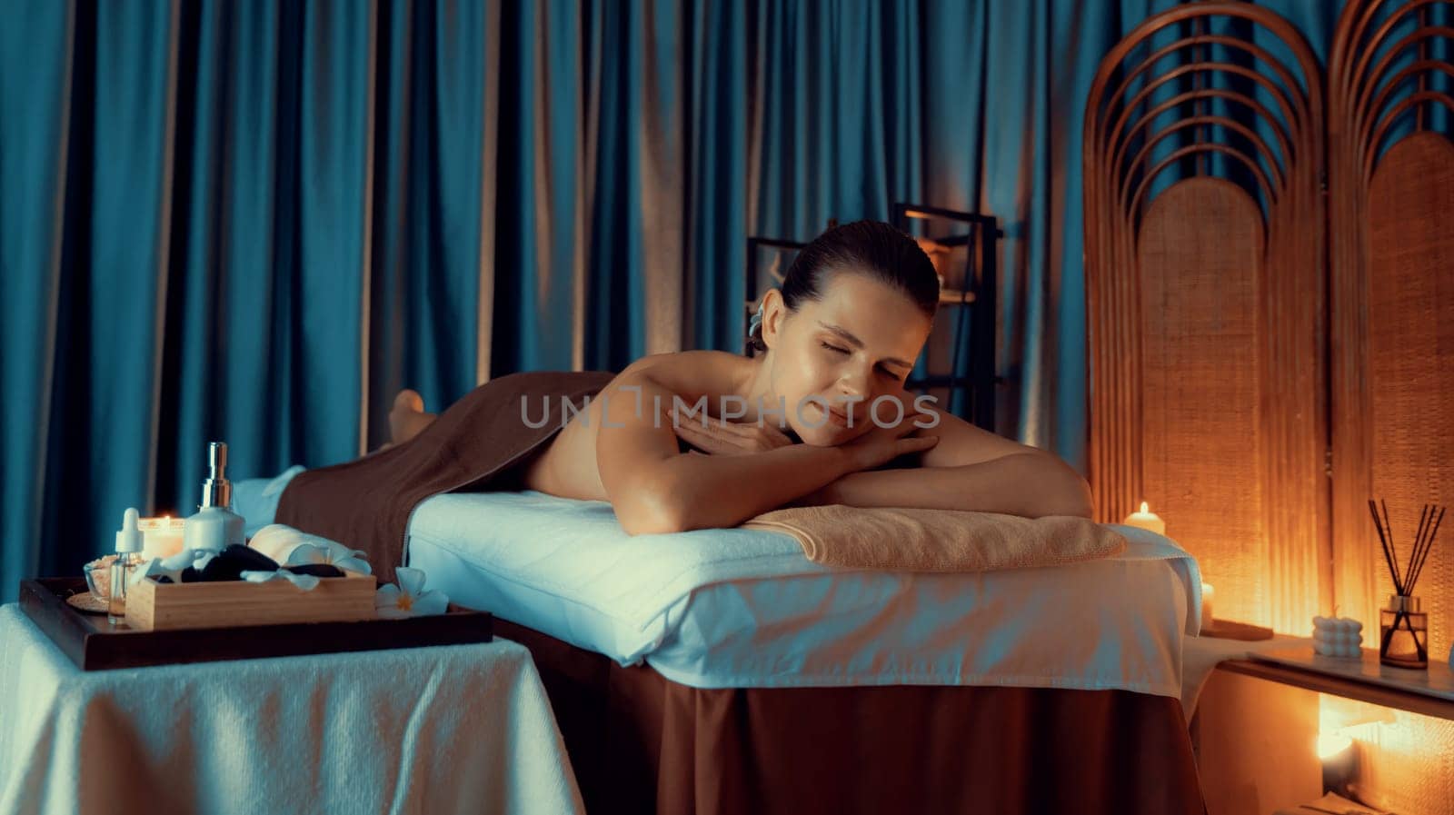 Caucasian woman customer enjoying relaxing anti-stress spa massage and pampering with beauty skin recreation leisure in warm candle lighting ambient salon spa at luxury resort or hotel. Quiescent