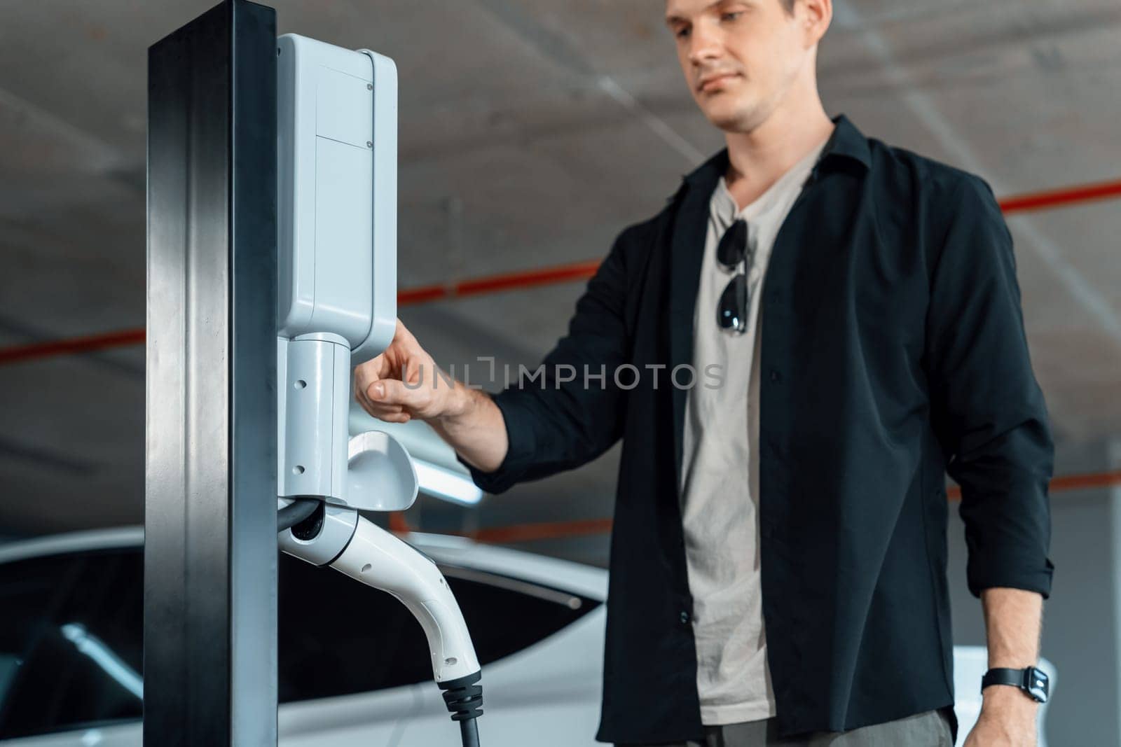 Young man travel with EV electric car to shopping center parking lot charging in downtown city showing urban sustainability lifestyle by green clean rechargeable energy of electric vehicle innards