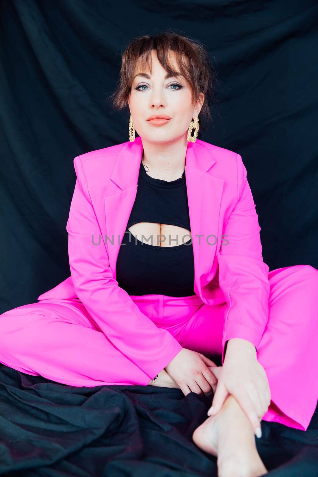 Woman sitting in bright suit on black background by Simakov