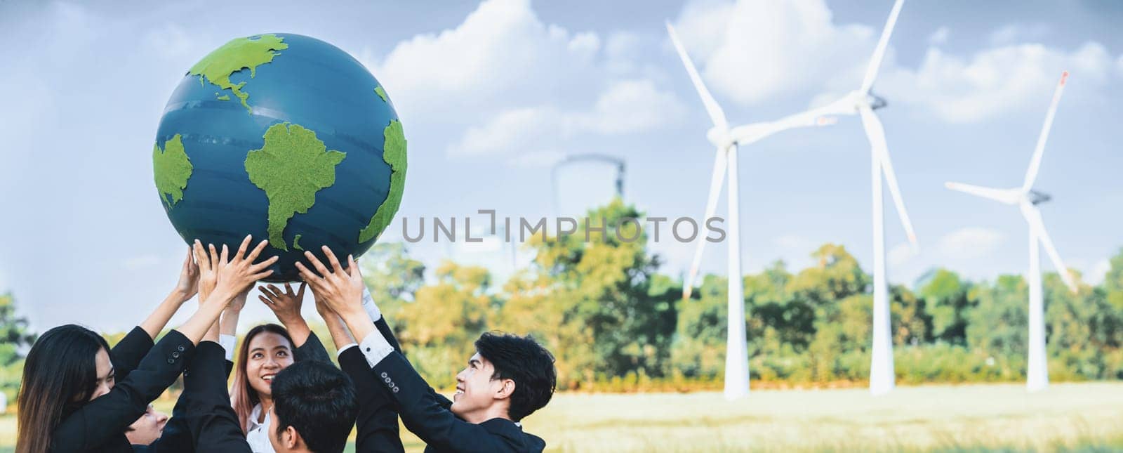 Earth day concept with big Earth globe held by asian business people team promoting environmental awareness using clean sustainable and renewable energy with wind turbine for greener future. Gyre