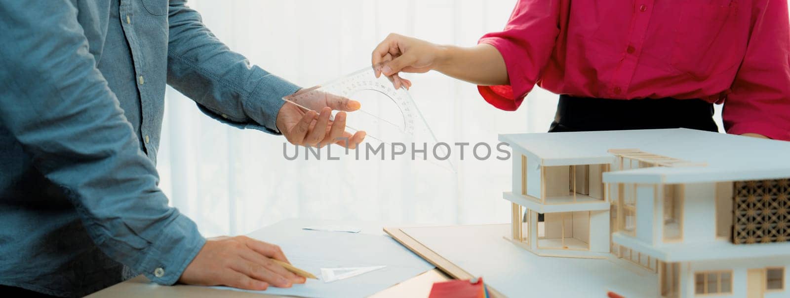 Young smart architect sends architectural equipment to project manager for measuring a house model and architectural equipment placed on meeting table. Creative design and teamwork. Variegated.