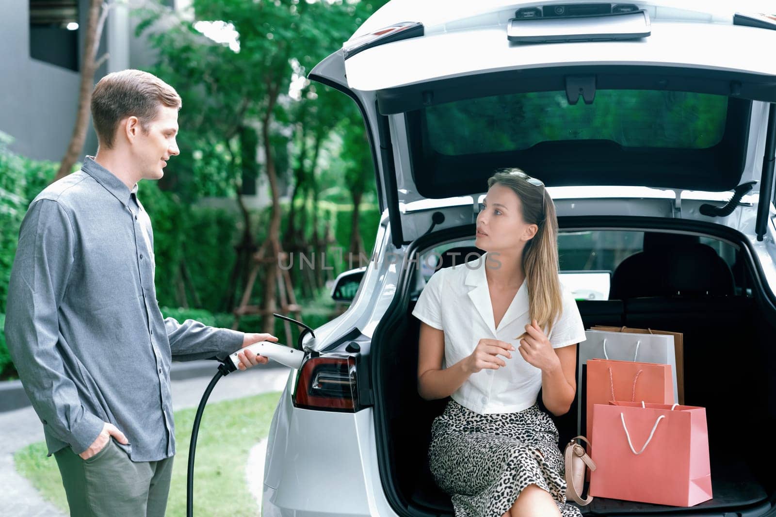 Young couple travel with EV electric car in green sustainable city innards by biancoblue