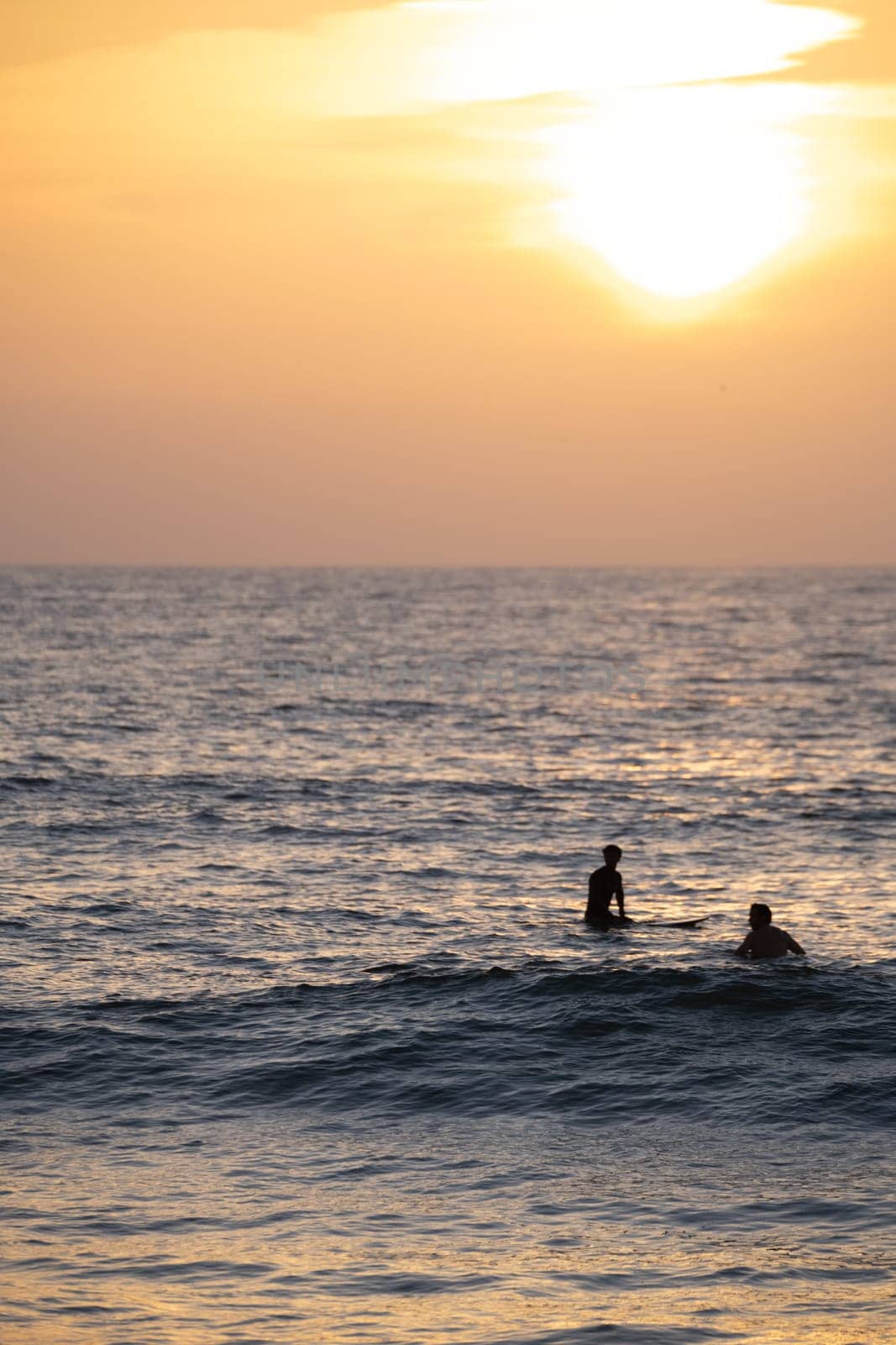 Surfer silhouettes in the Atlantic Ocean from Furadouro Beach at sunset and golden hour, Ovar - Portugal.