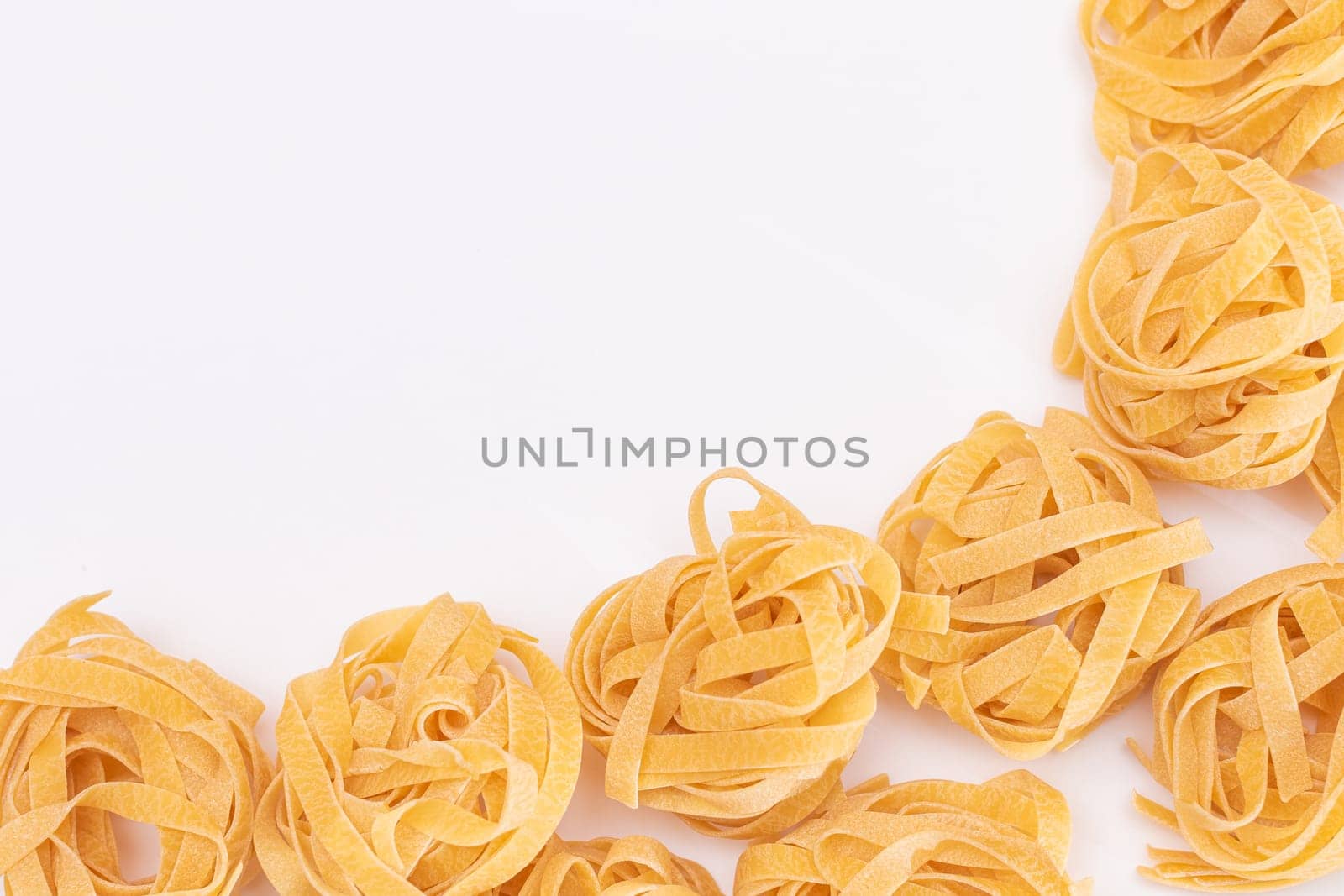 Classic Italian Raw Egg Fettuccine with Copy Spase on White Background. Dry Twisted Uncooked Pasta. Italian Culture and Cuisine. Raw Golden Macaroni Pattern