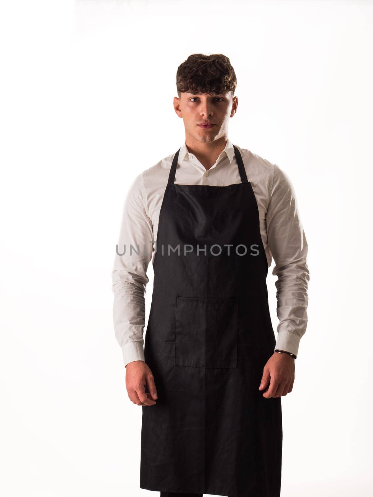 Young chef or waiter posing, wearing black apron and white shirt isolated on white background