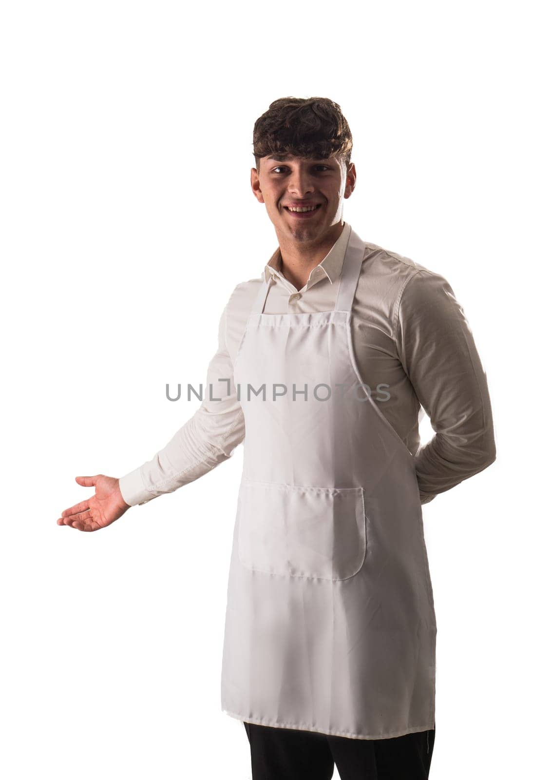 Young chef or waiter posing, wearing white apron and white shirt isolated on white background, welcoming people into the restaurant with a smile