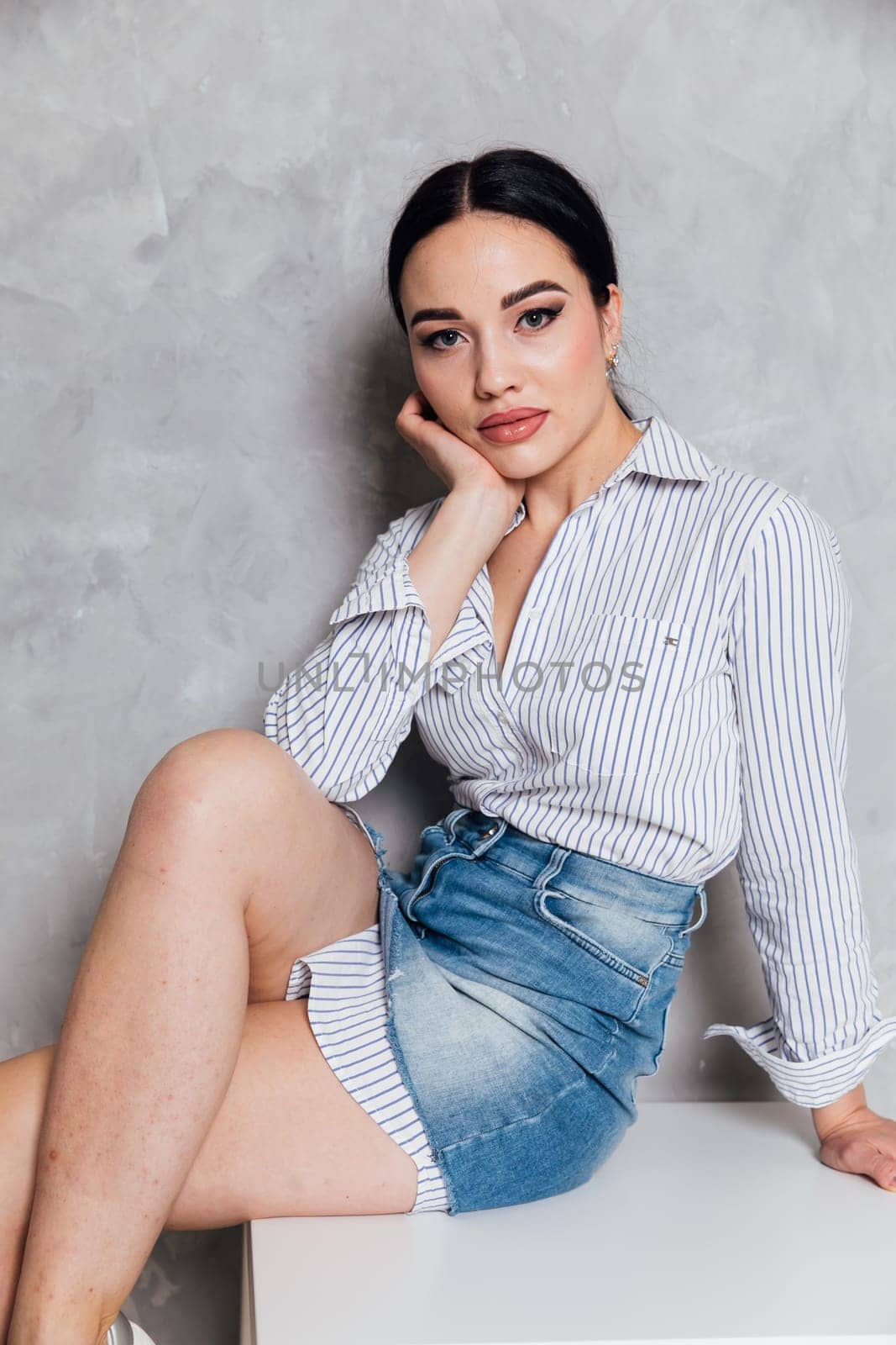 Beautiful fashionable woman in denim skirt posing in studio on gray background by Simakov