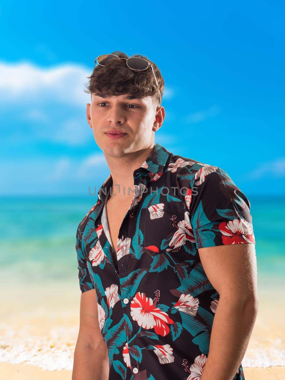 Attractive, muscular young man smiling, wearing open hawaian style shirt on a beach