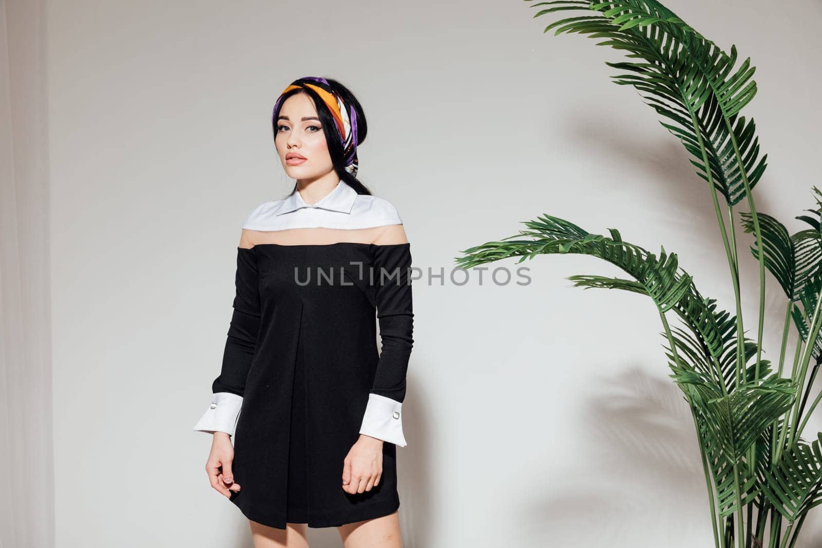 woman in black dress posing on white background near indoor flower