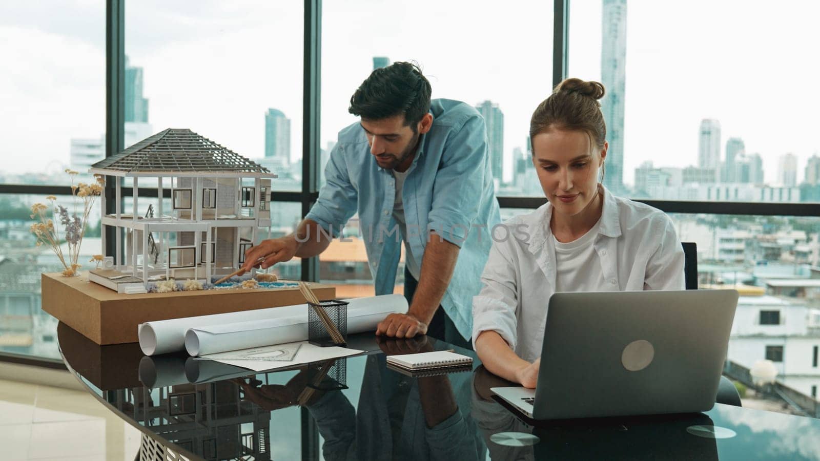 Smart engineer inspect house model while colleague using laptop. Tracery by biancoblue