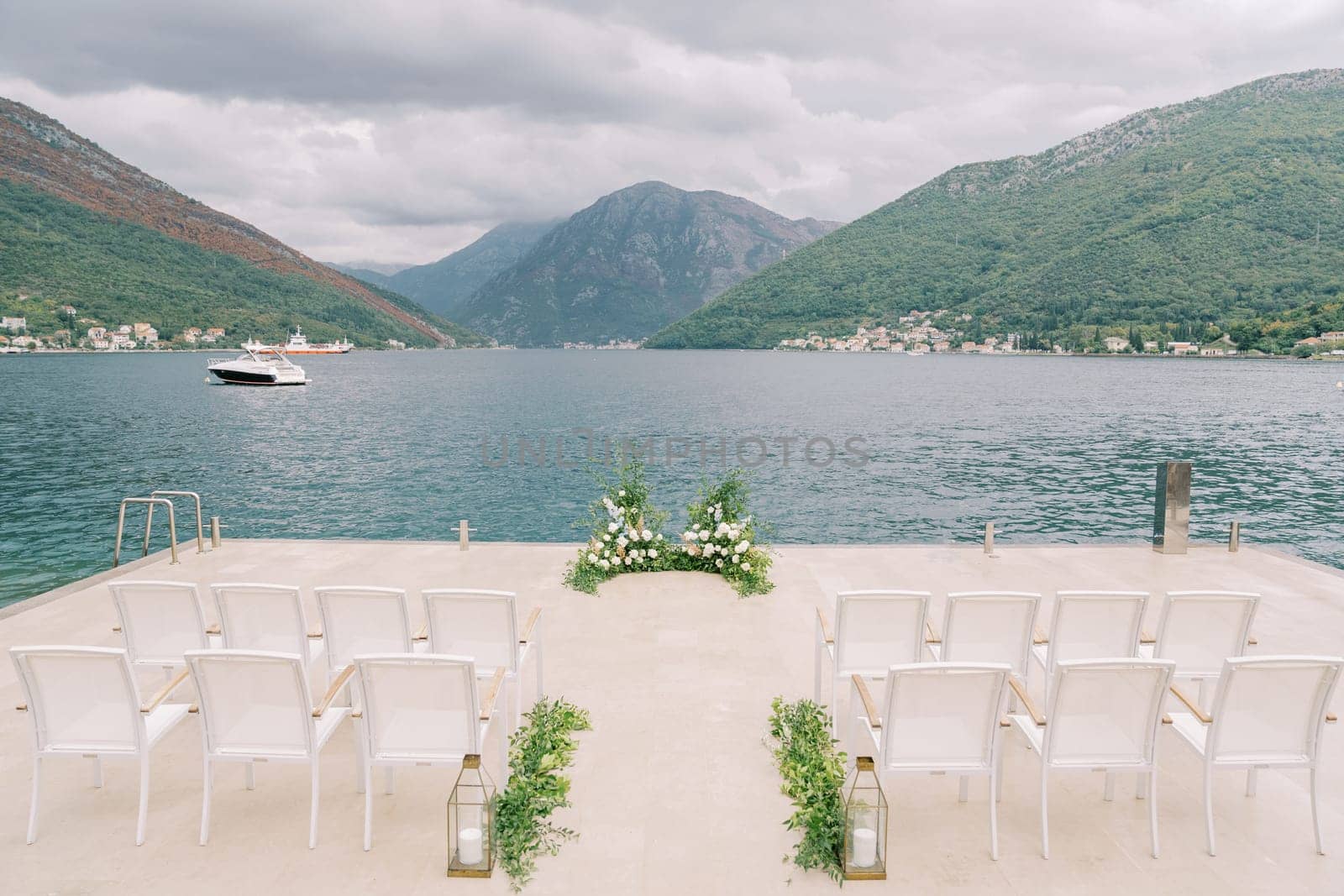 Rows of chairs stand on the pier in front of a floor wedding arch by Nadtochiy