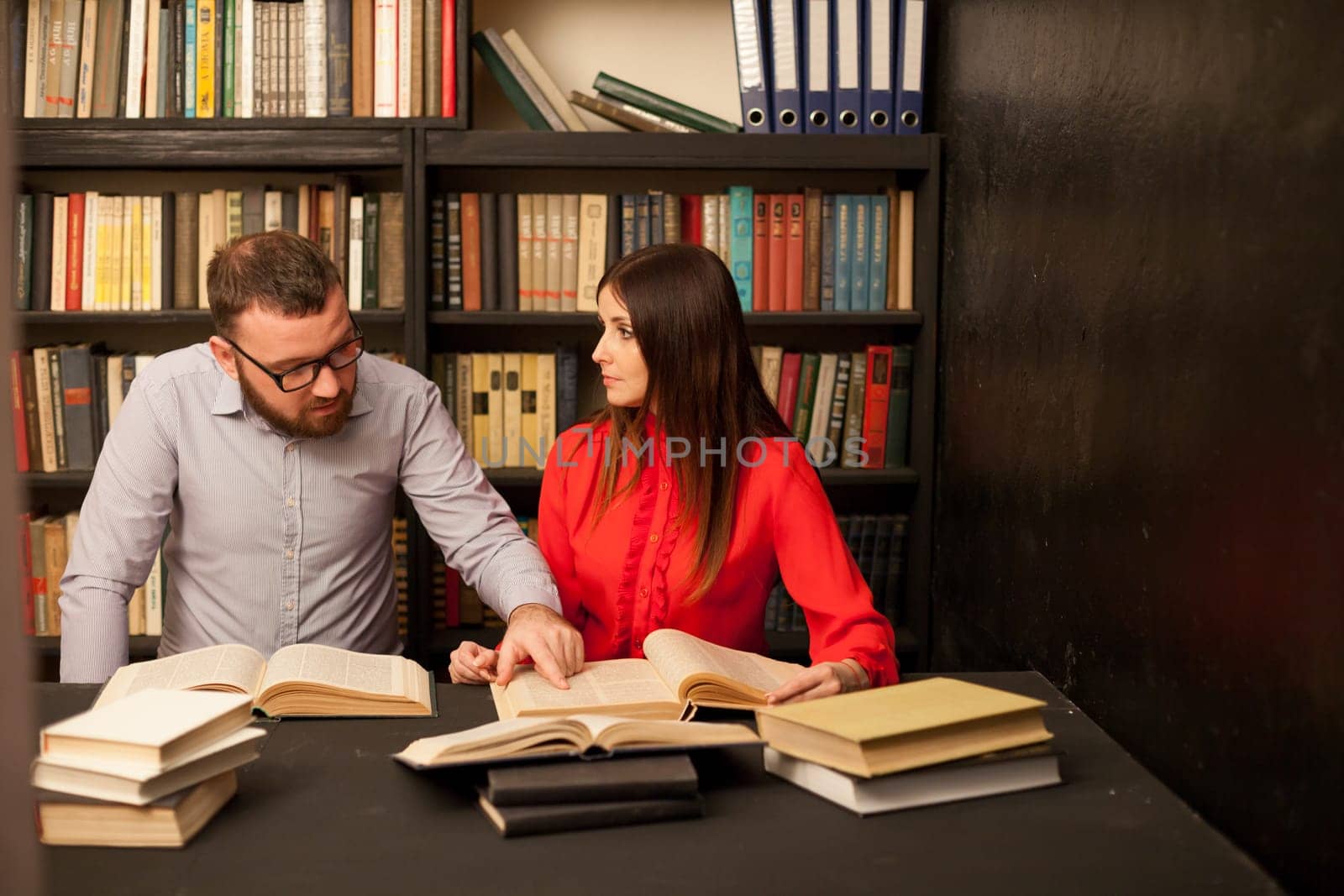 a man and a woman read a lot of books in the library by Simakov