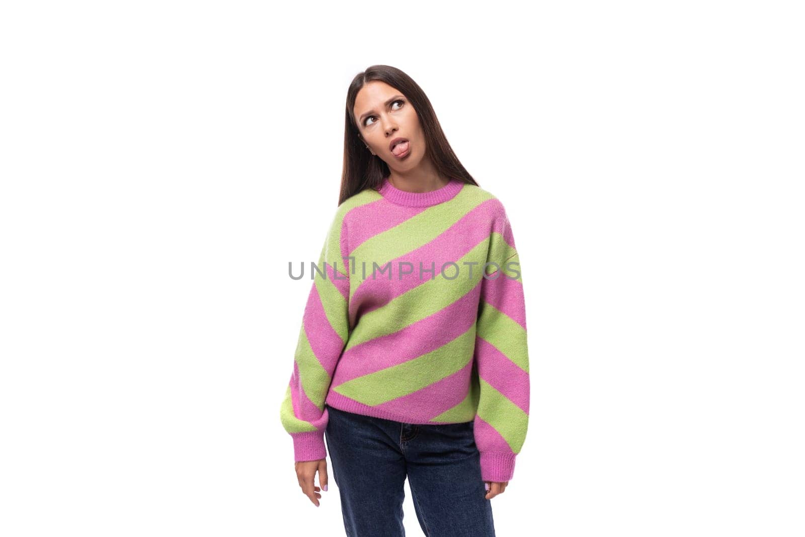 young slender caucasian woman with straight black hair dressed in a striped pink pullover shows her tongue on a white background.