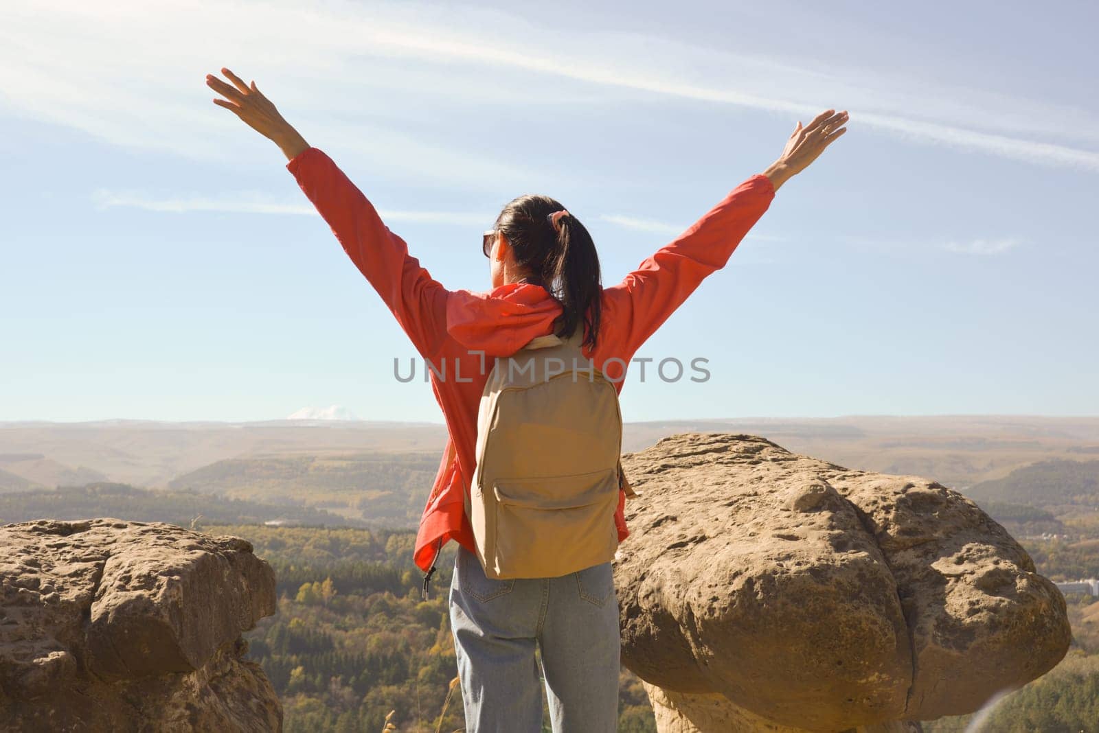 Active young woman with backpack hiking in the mountains with her arms raised up by Ekaterina34