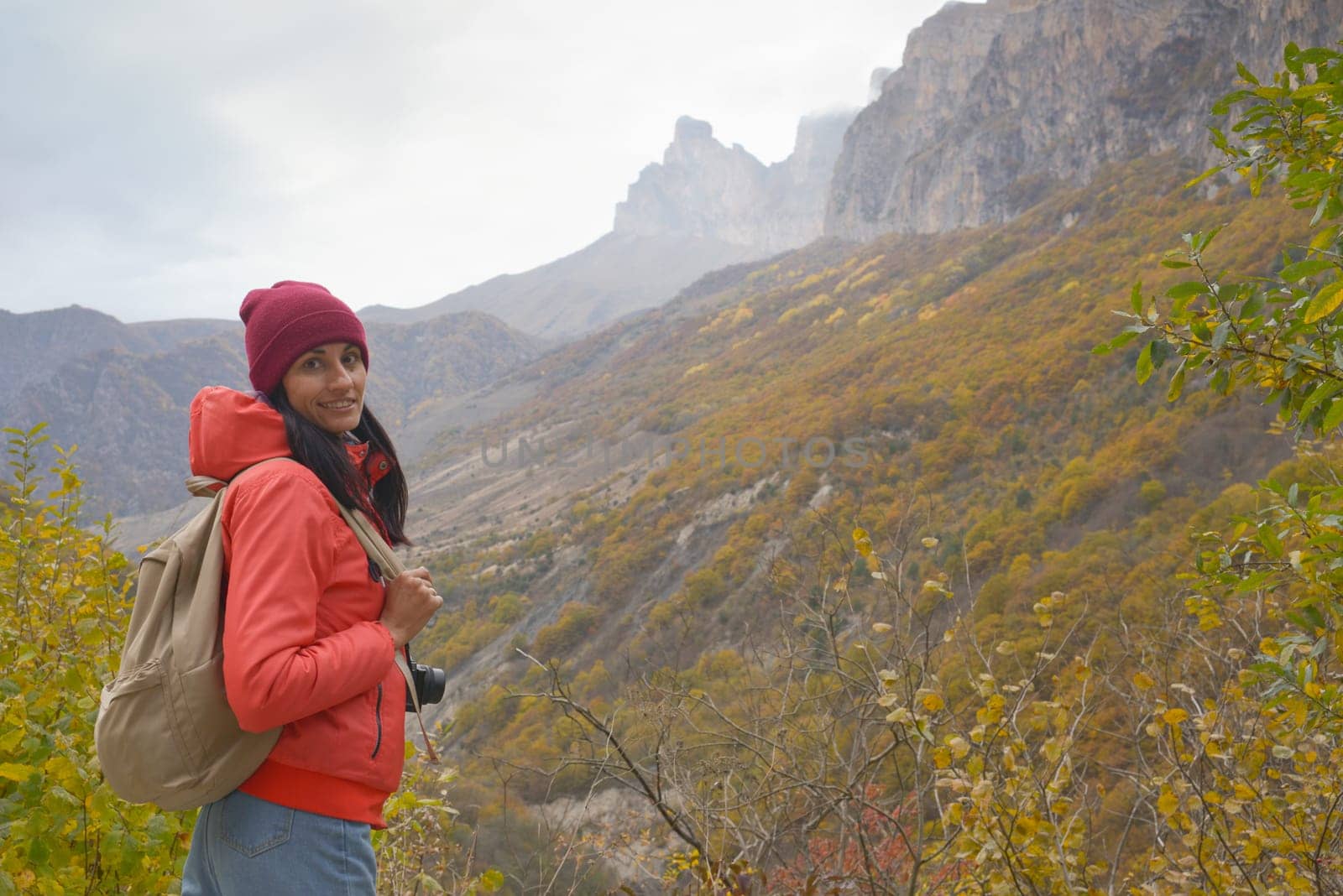 A free woman traveler with a backpack stands in the mountains and enjoys the beautiful scenery on a foggy autumn day. Adventure travel and success concept.
