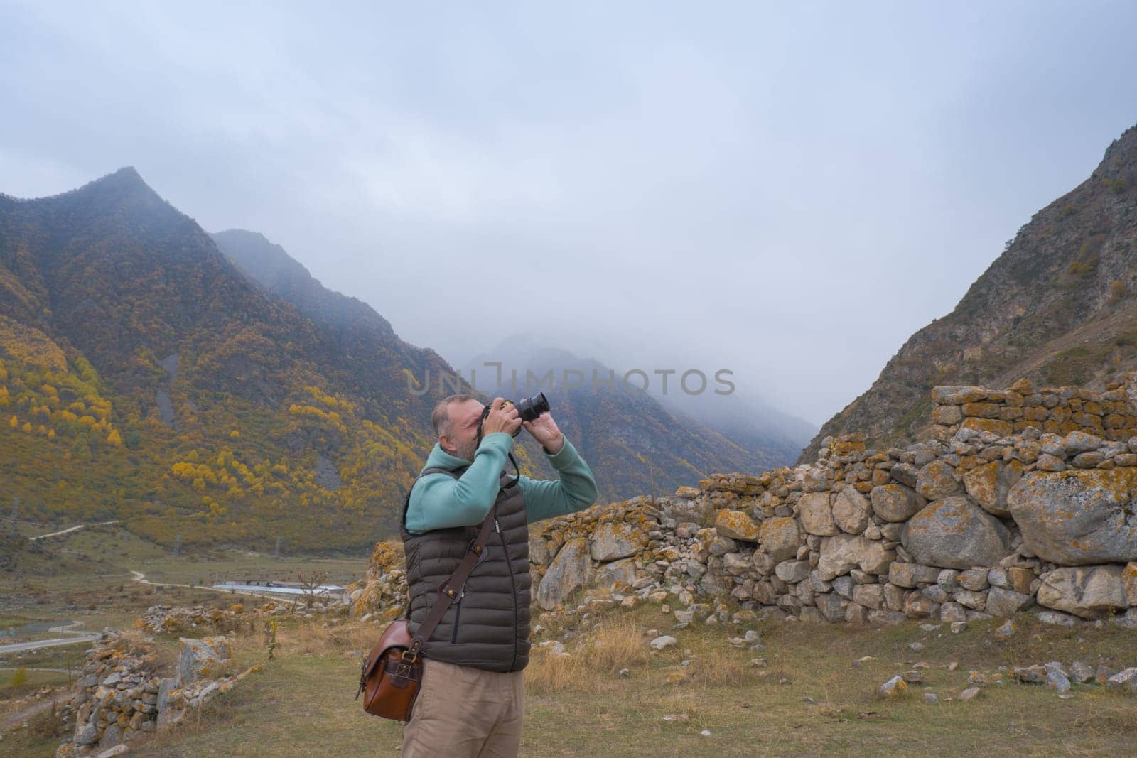 A male tourist takes pictures of a beautiful autumn mountain foggy landscape using a camera. by Ekaterina34
