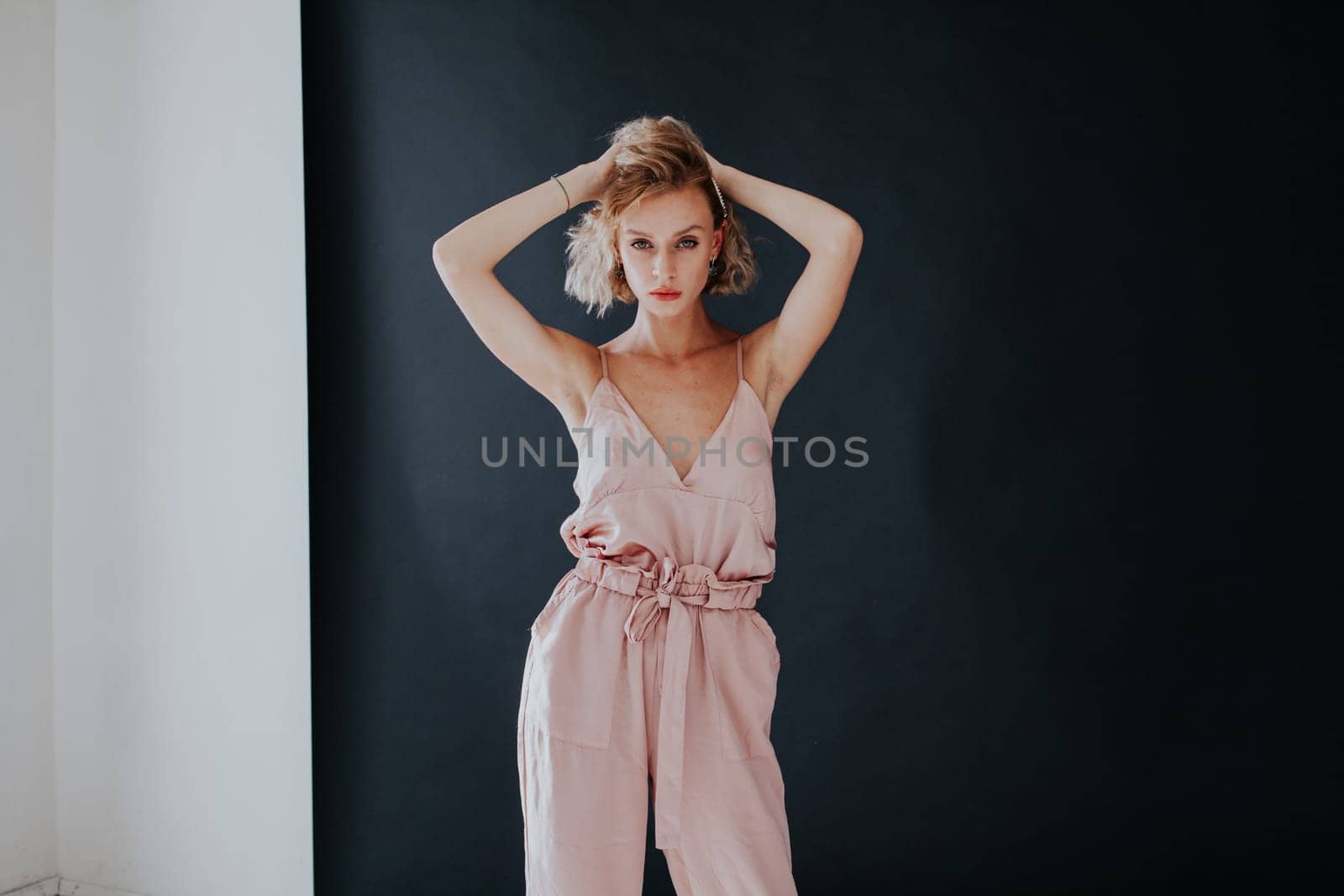 portrait of a beautiful fashionable woman in a pink jumpsuit against a black background