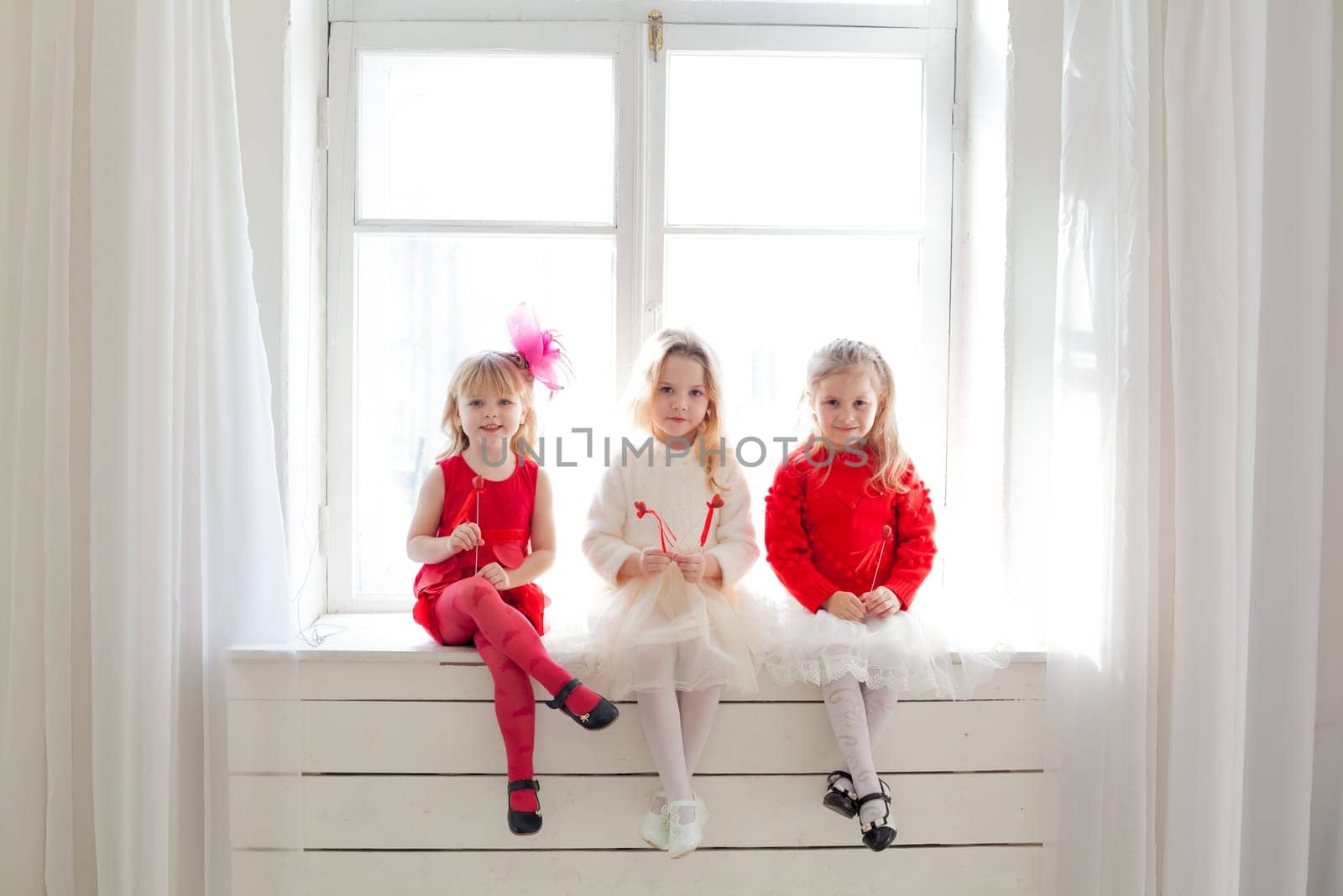 three girls in red and white clothes on holiday sit by the window
