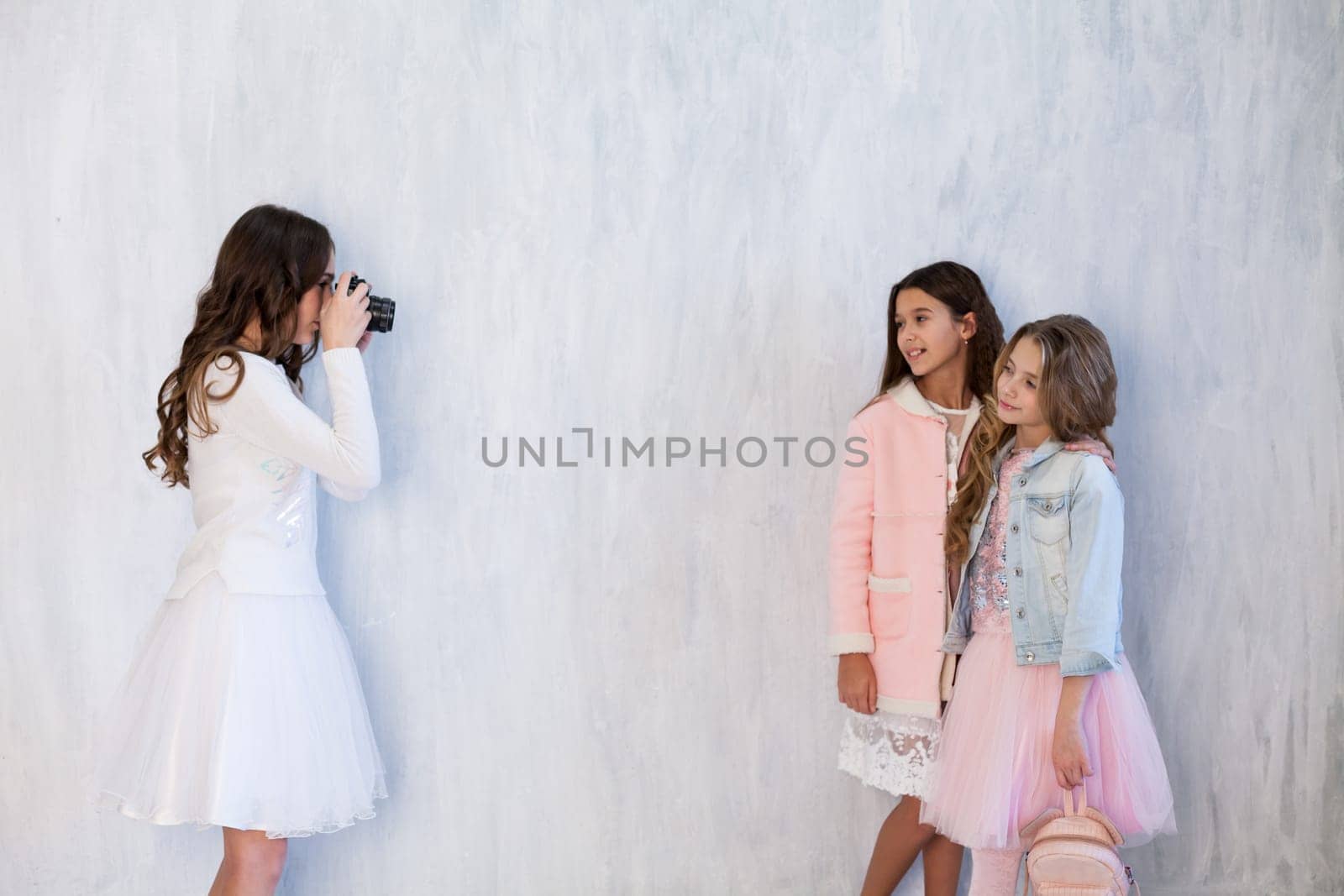 Three beautiful fashionable girls in white pink clothes at the photo shoot are photographed