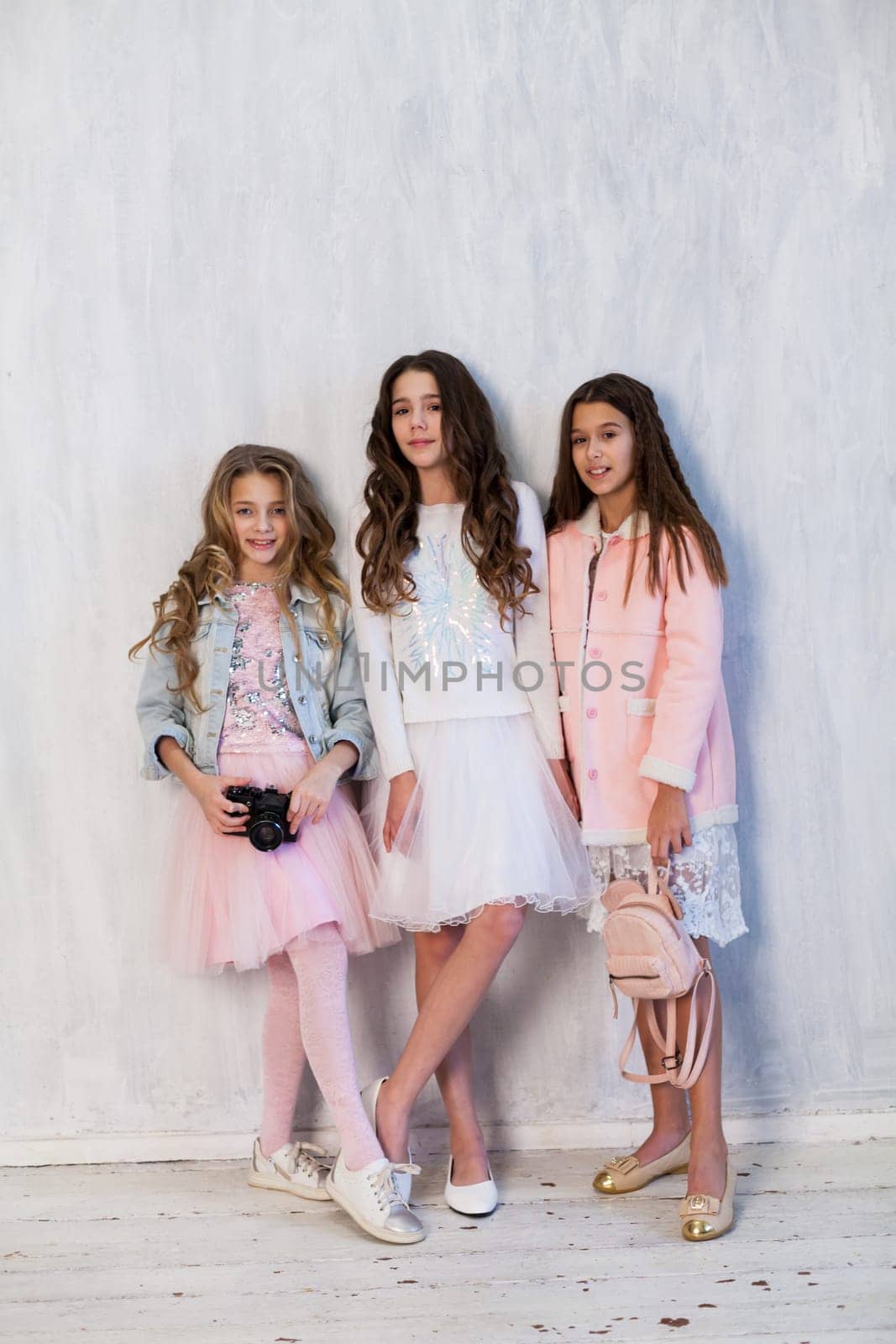 Three beautiful fashionable girls in white pink clothes at the photo shoot are photographed