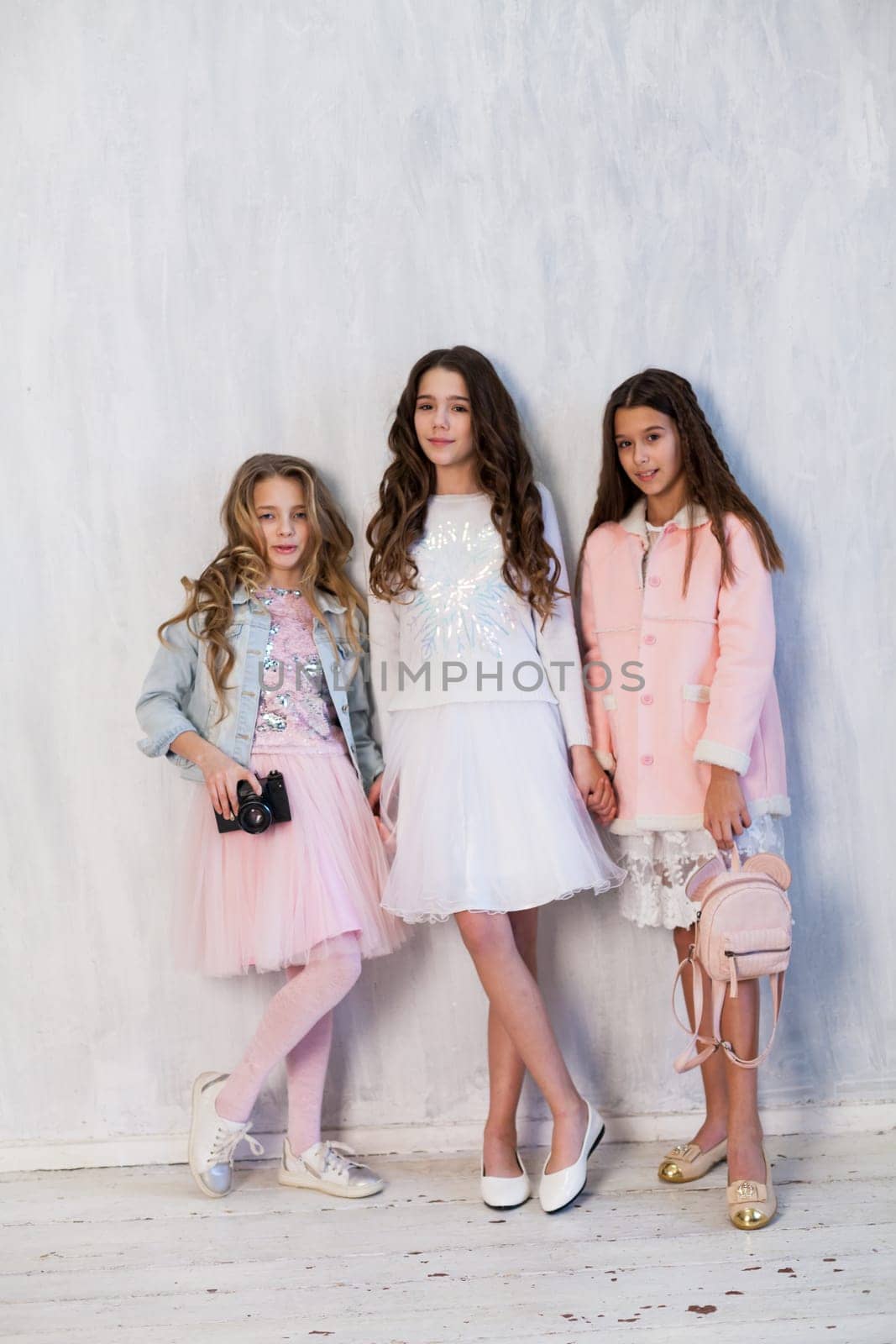 Three beautiful fashionable girls in white pink clothes at the photo shoot are photographed