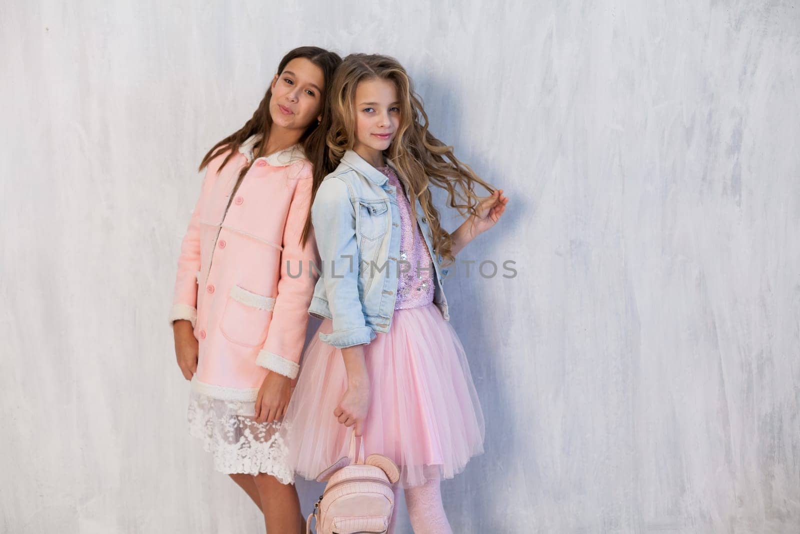 portrait of two beautiful girls in white pink clothes on a gray background