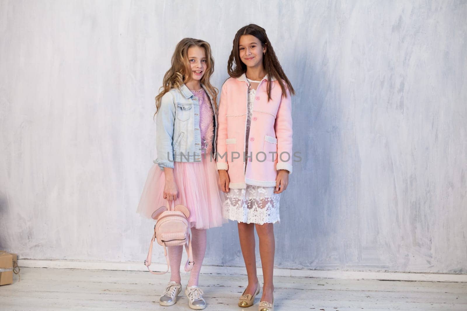 portrait of two beautiful girls in white pink clothes on a gray background