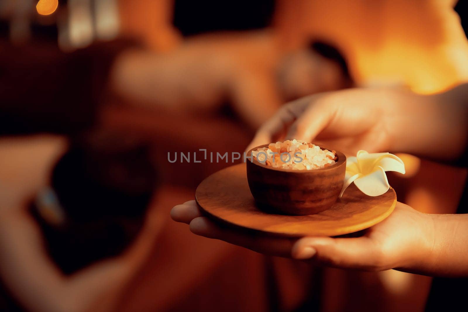 Masseur holding spa salt while couple customer having exfoliation treatment in luxury spa salon with warmth candle light ambient. Salt scrub beauty treatment in Health spa body scrub. Quiescent