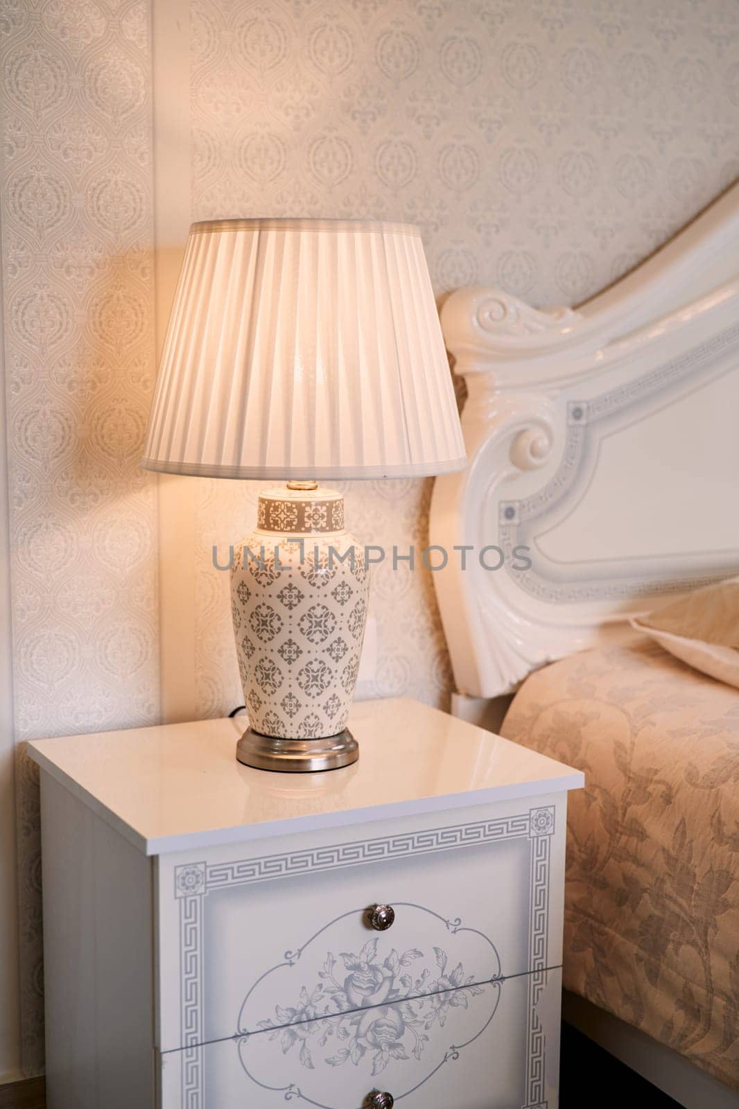 Luminous lamp with a lampshade stands near the bed on the nightstand. High quality photo