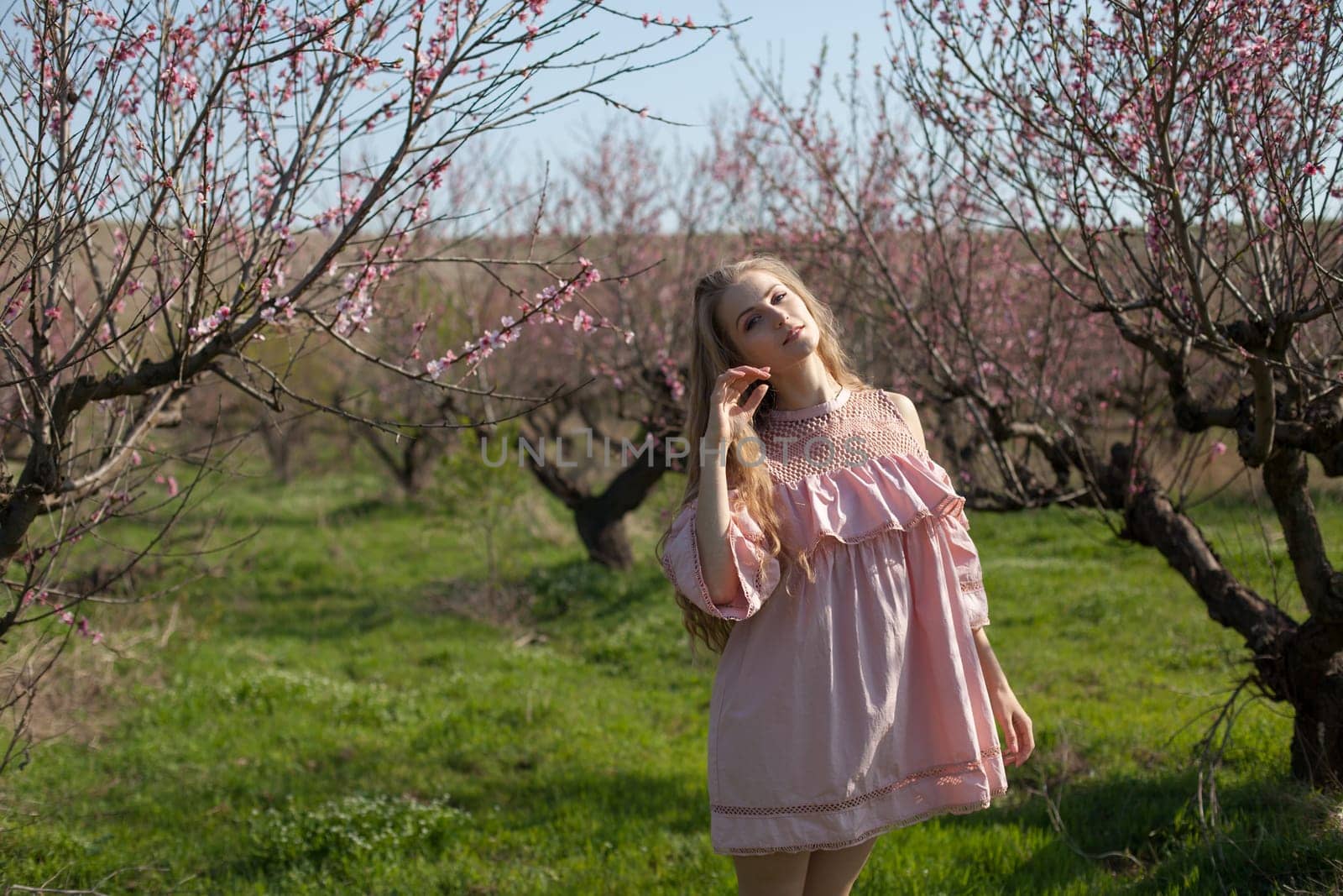 Beautiful happy blonde woman in pink dress walks through the flowering garden in spring