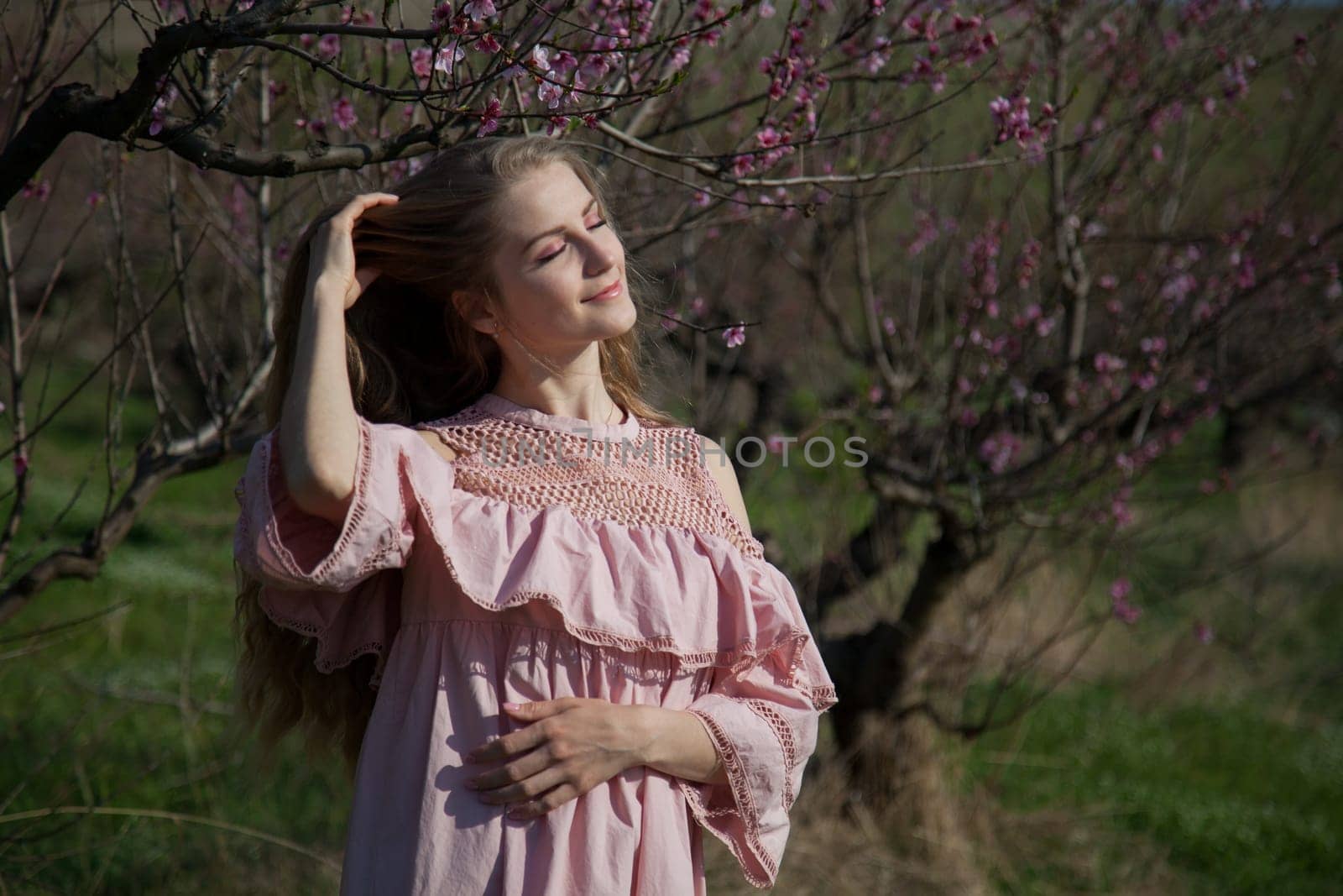 Beautiful happy blonde woman in pink dress walks through the flowering garden in spring