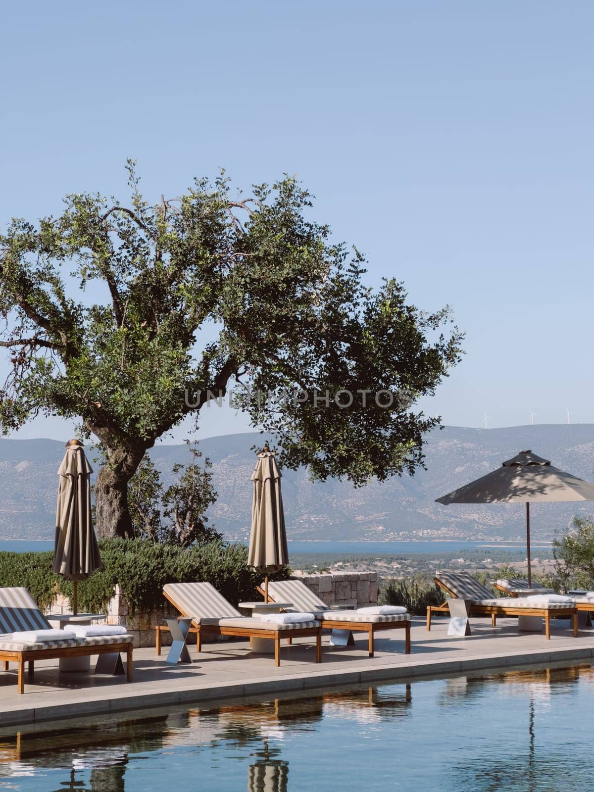 Sun loungers and sun umbrellas stand by the pool against the backdrop of the mountains. Hotel Amanzoe, Greece. High quality photo