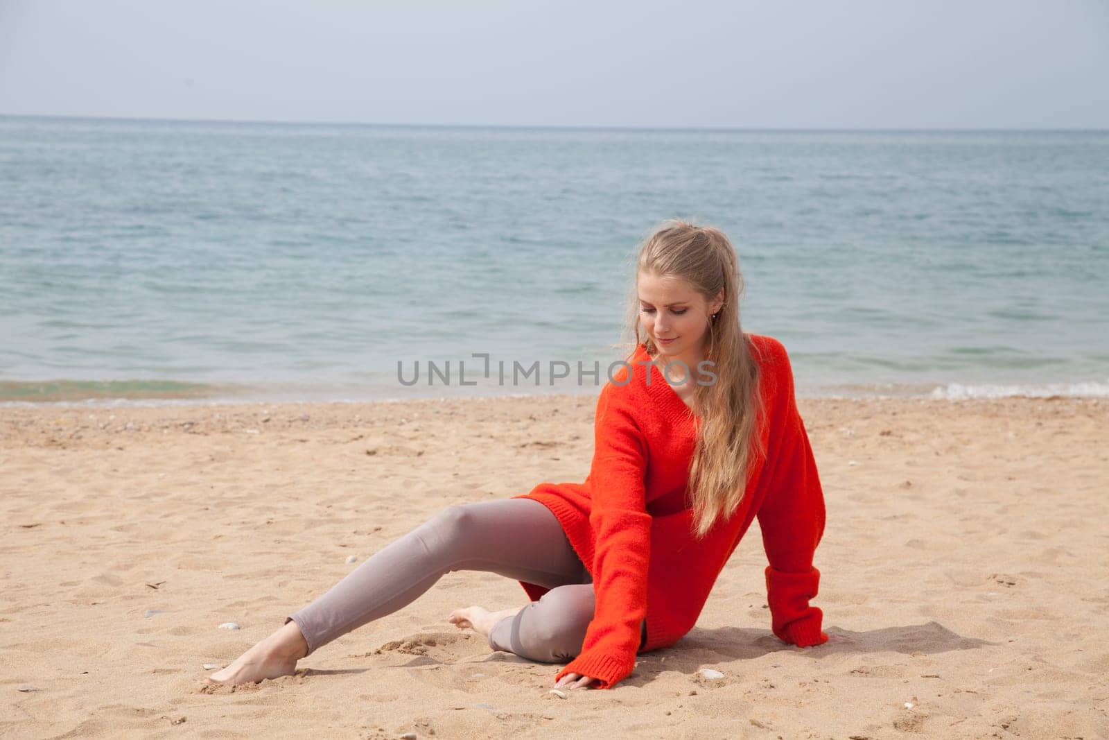 blonde woman sits alone on the beach by the sea