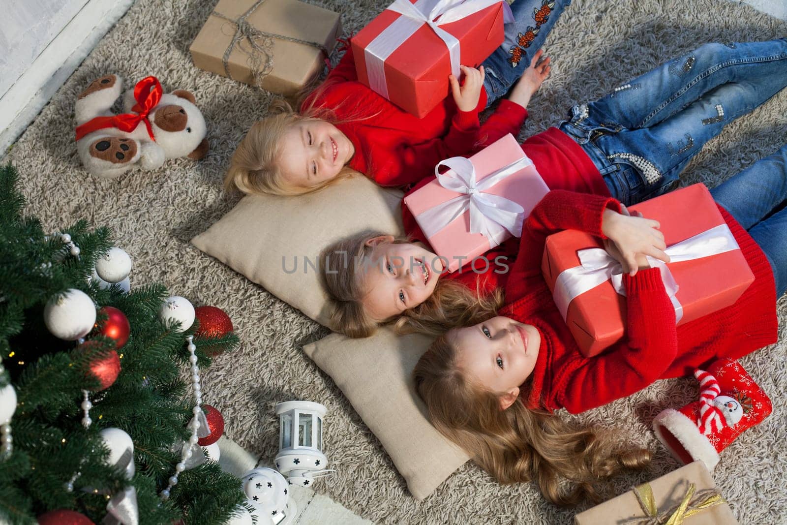 Three little girl girlfriends open gifts at the Christmas tree new year winter