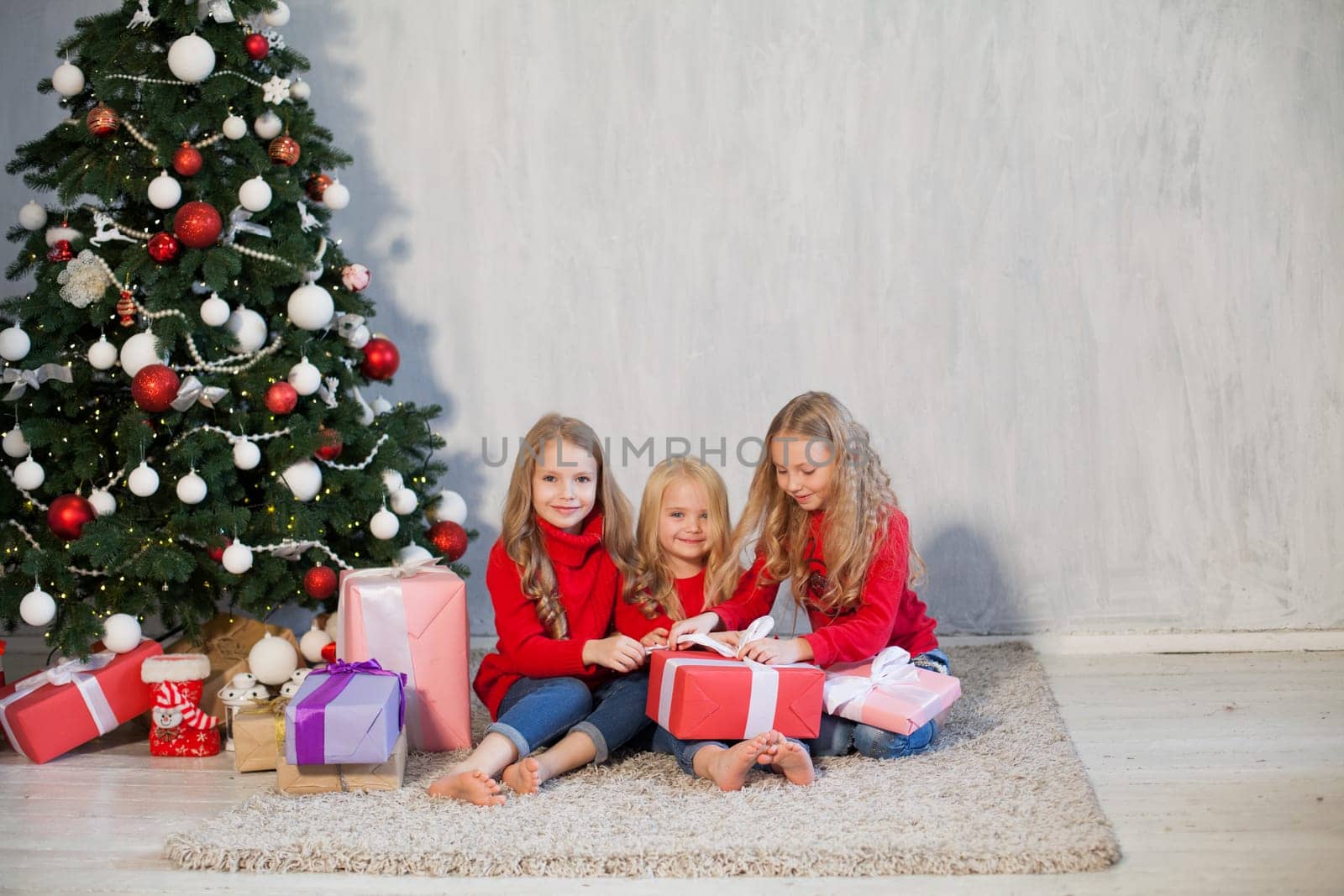 Three little girls open gifts at the Christmas tree new year winter by Simakov