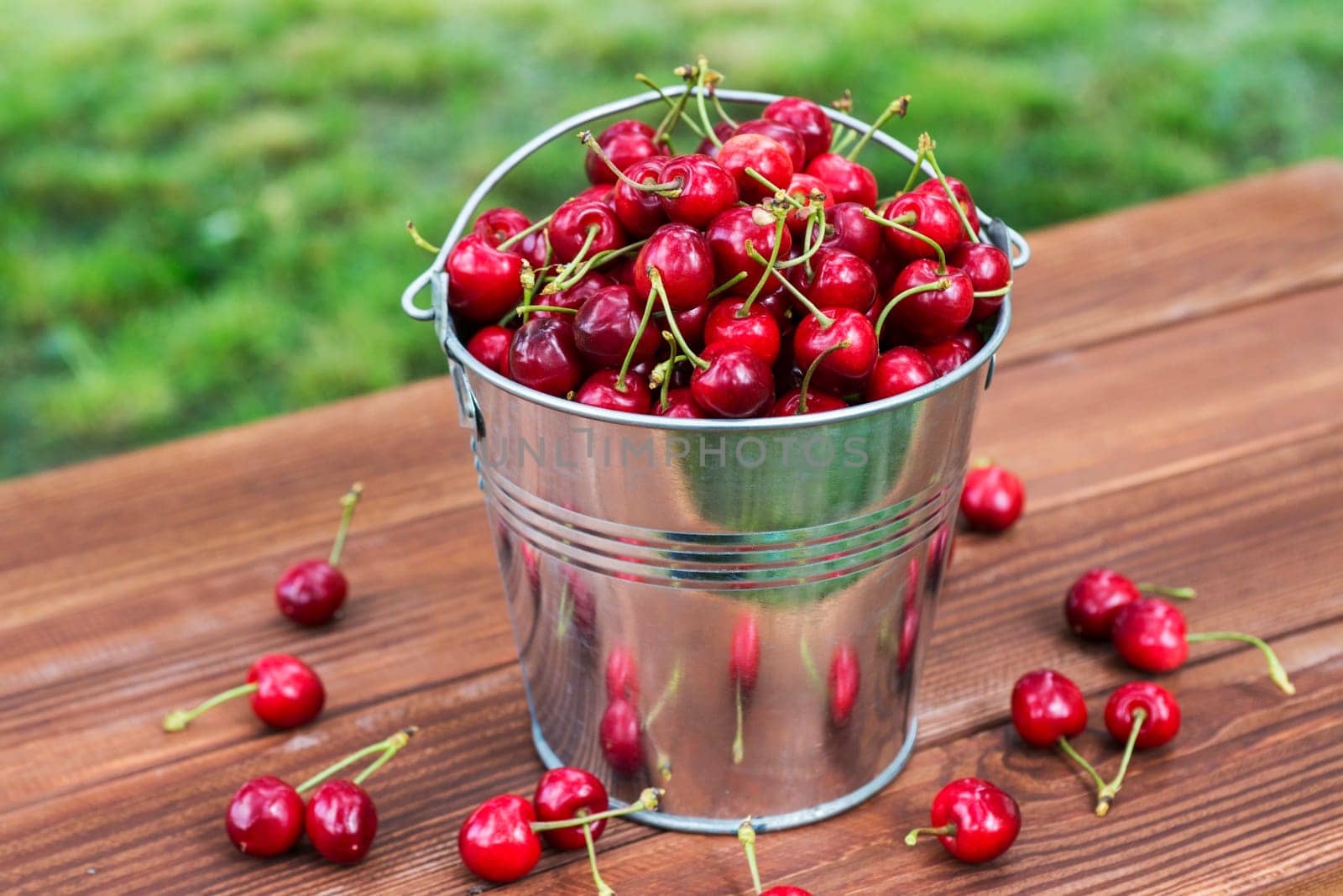 Fresh red ripe cherry in a bucket on the wooden background. Ripe red cherries in the metal bucket on a wooden background.