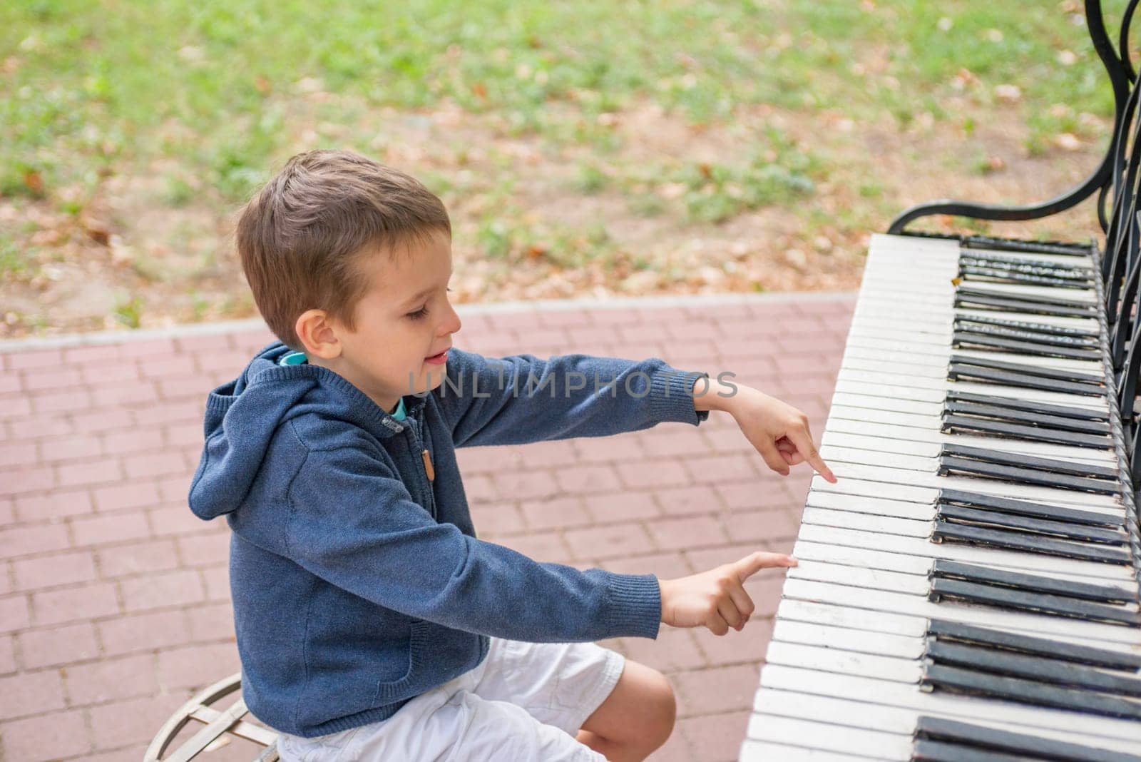 A little boy plays the street piano in the summer. Child playing piano by andreyz