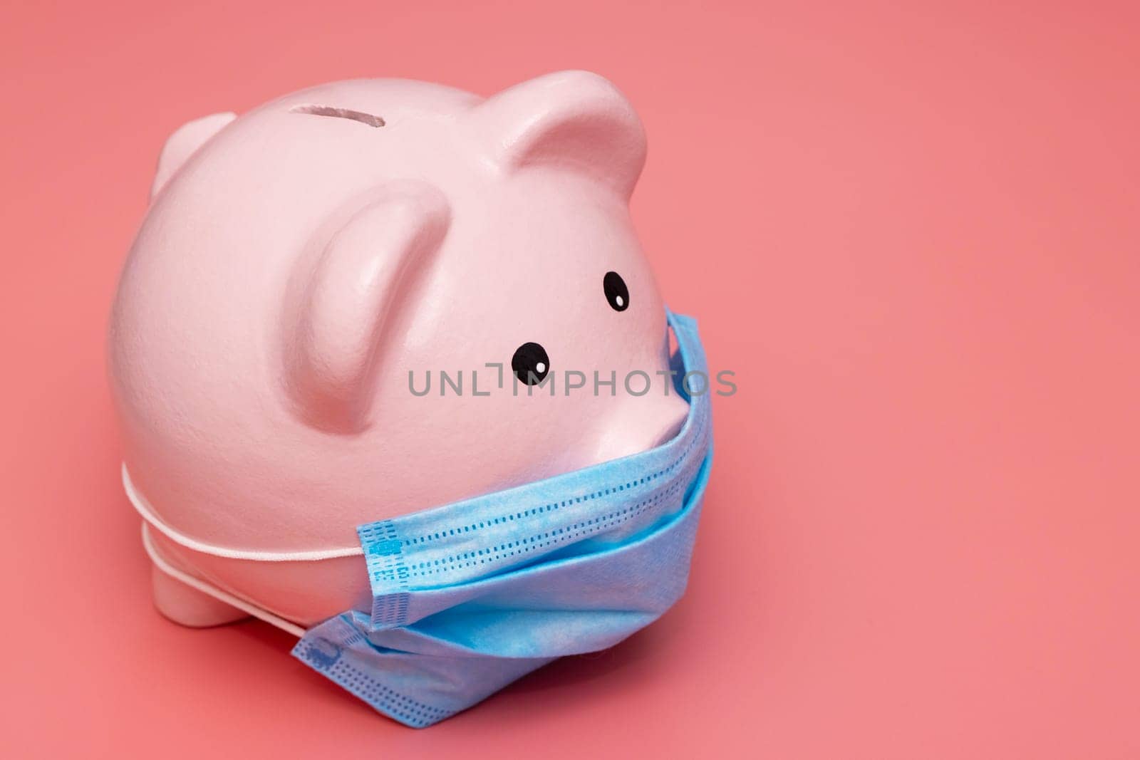 Concept of economic crisis. Piggy bank with protective mask on pink background.