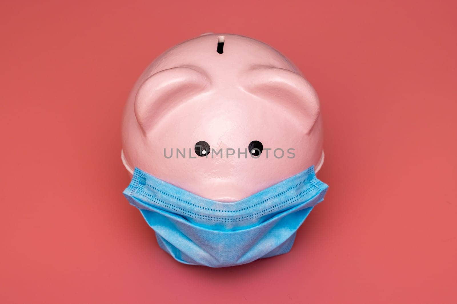 Concept of economic crisis. Piggy bank with protective mask on pink background.